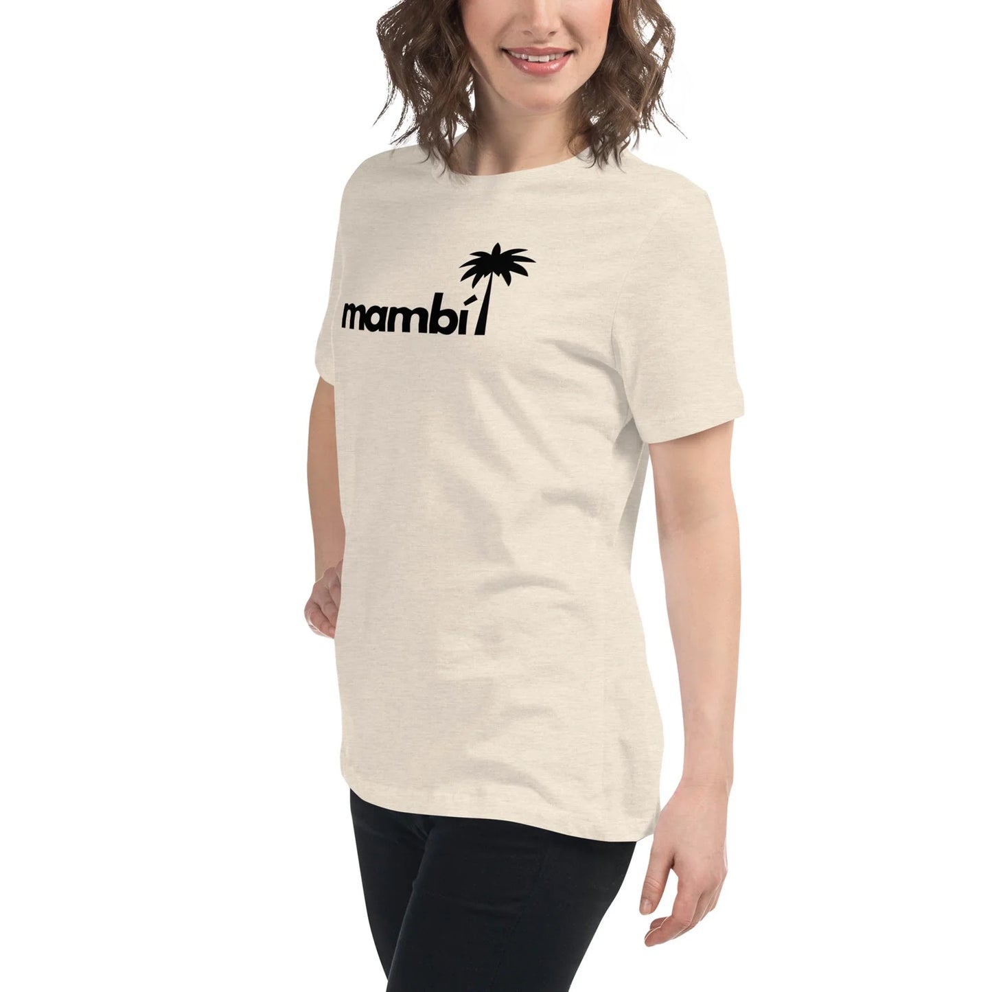 A smiling woman with wavy brown hair wears a light-colored t-shirt featuring the word Mambí and a black palm tree graphic. She is standing and posing against a white background.