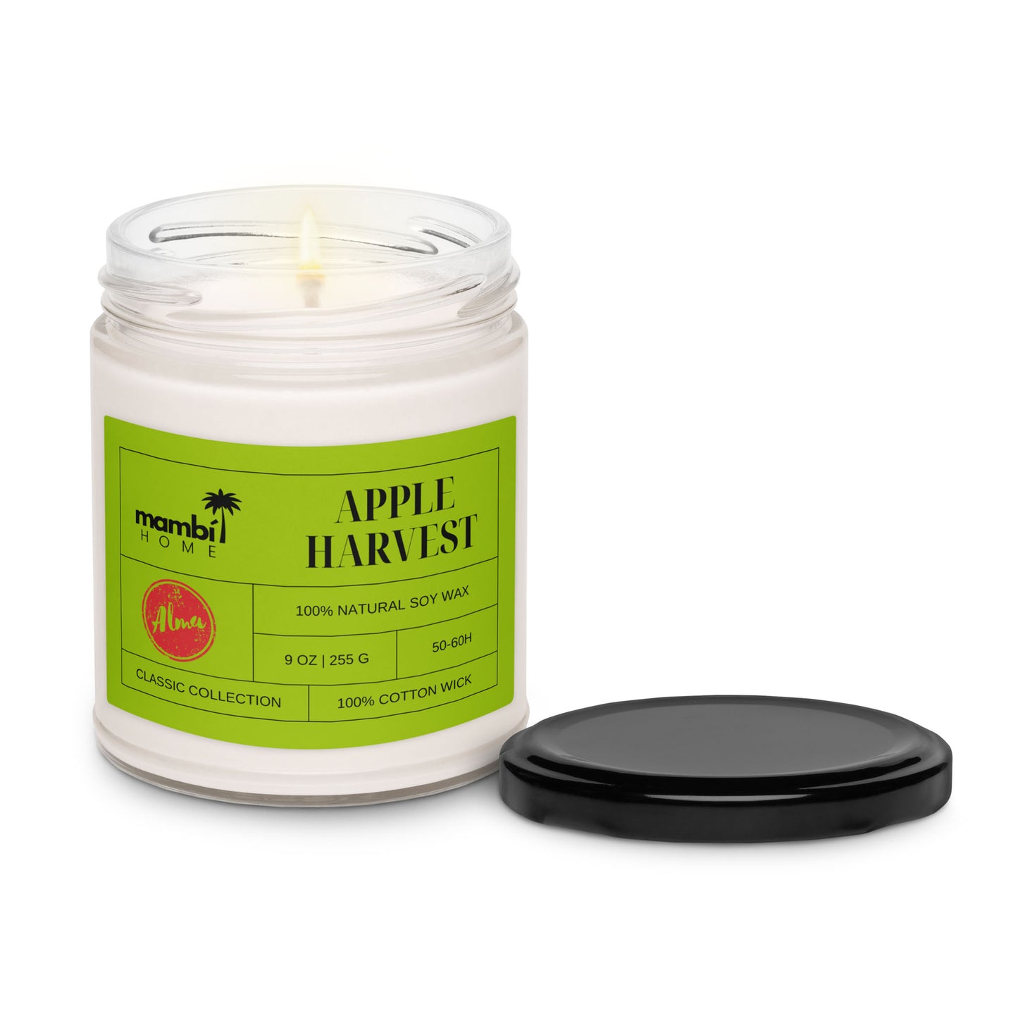 A lit white scented soy candle in a clear glass jar labeled Apple Harvest with a green label, next to a black lid, on a white background. The label details scent, size, and burn time.