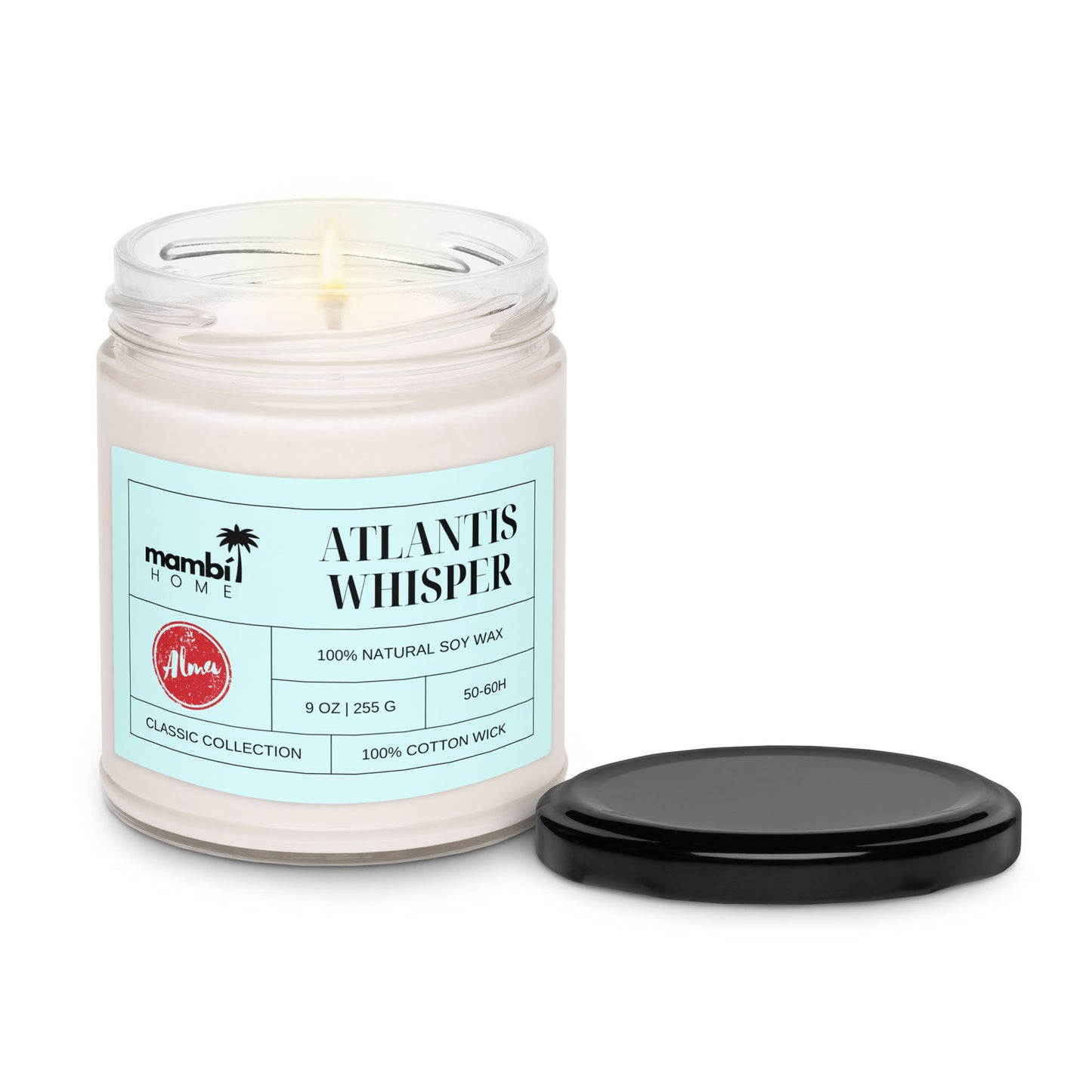 A lit white scented soy candle in a clear glass jar labeled Atlantis Whisper by mambi HOME, with the black lid resting beside it. The label highlights it as 100% natural soy wax with a cotton wick, ensuring long burn time candles.