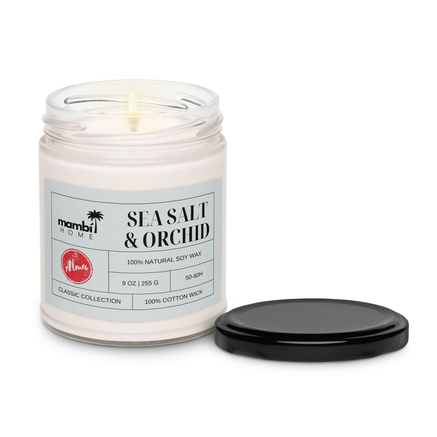A lit white scented soy candle in a glass jar labeled Sea Salt & Orchid from Mambi Home, with a black lid beside it. The label highlights its 100% natural soy wax and 100% cotton wick for an eco-friendly candle experience.