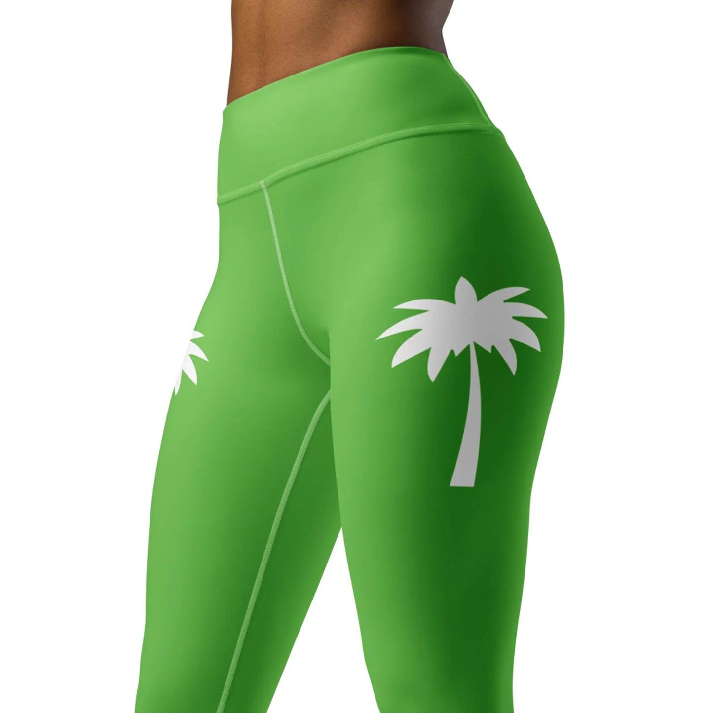 A model wears Printfuls Alpine High-Rise Yoga Leggings for women, featuring bright green fabric and white palm tree graphics on each hip, shown mid-torso to knees against a plain backdrop for an easy athleisure vibe.