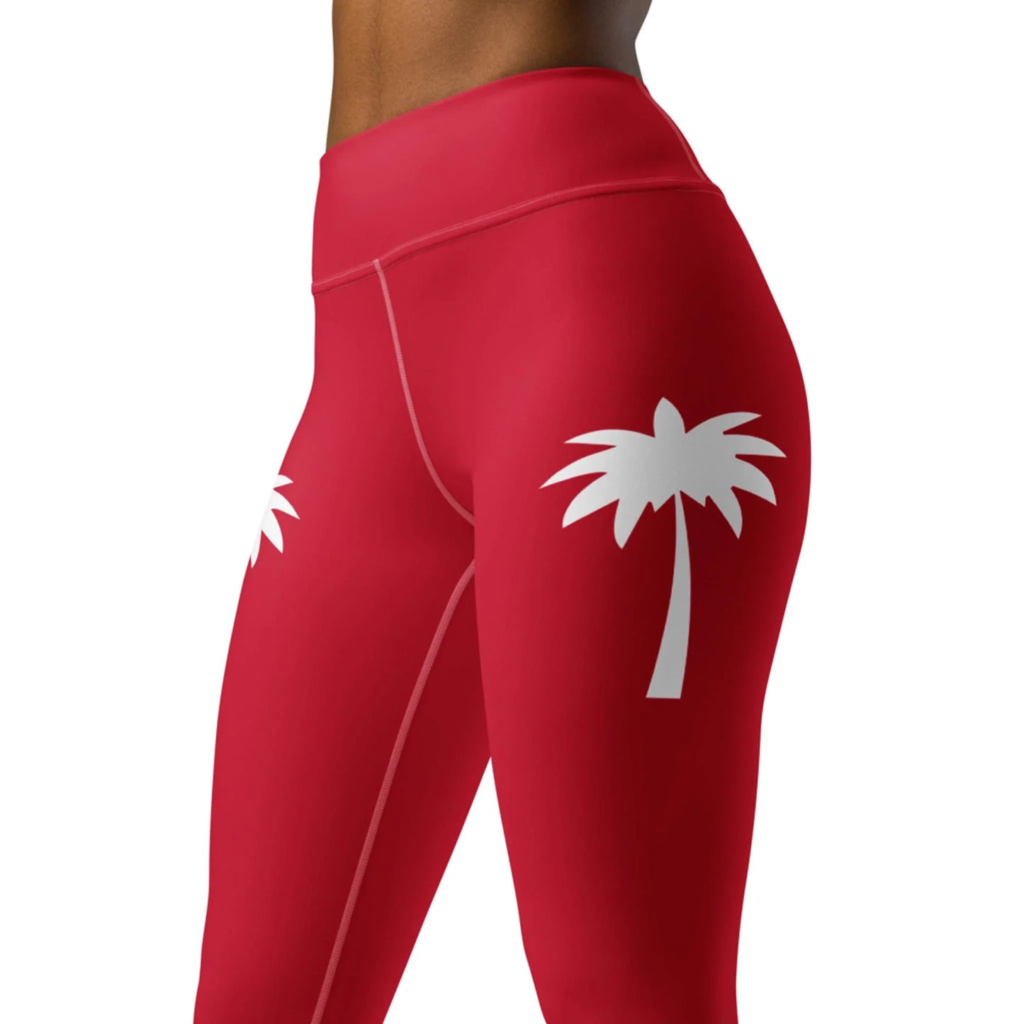 A model sports Printful’s Alpine High-Rise Yoga Leggings for women in red with white palm tree graphics on the outer thighs, showcased waist to mid-thigh for an effortless athleisure vibe against a plain backdrop.