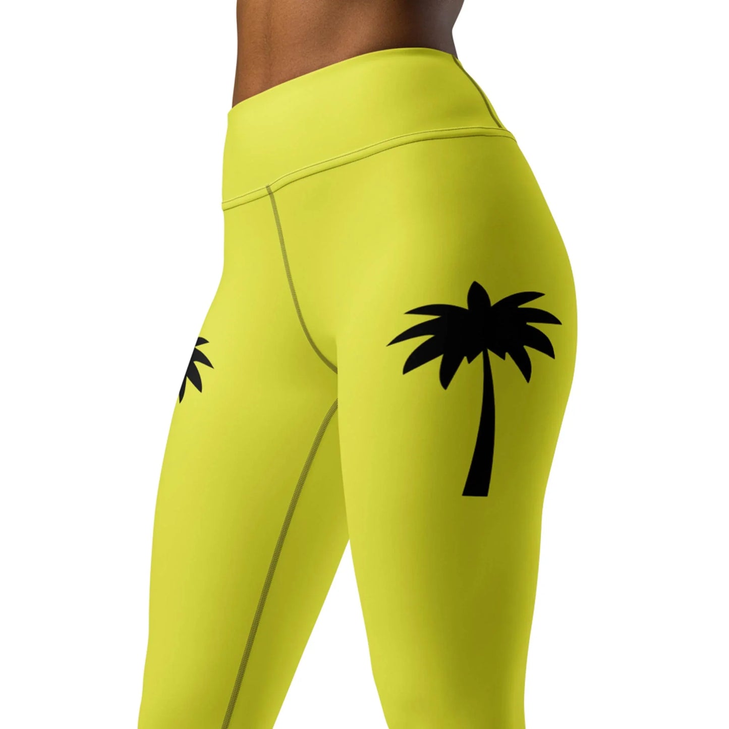 A person wearing Printfuls Alpine High-Rise Yoga Leggings for women in bright yellow with black palm tree prints from waist to mid-thigh creates a bold athleisure look.