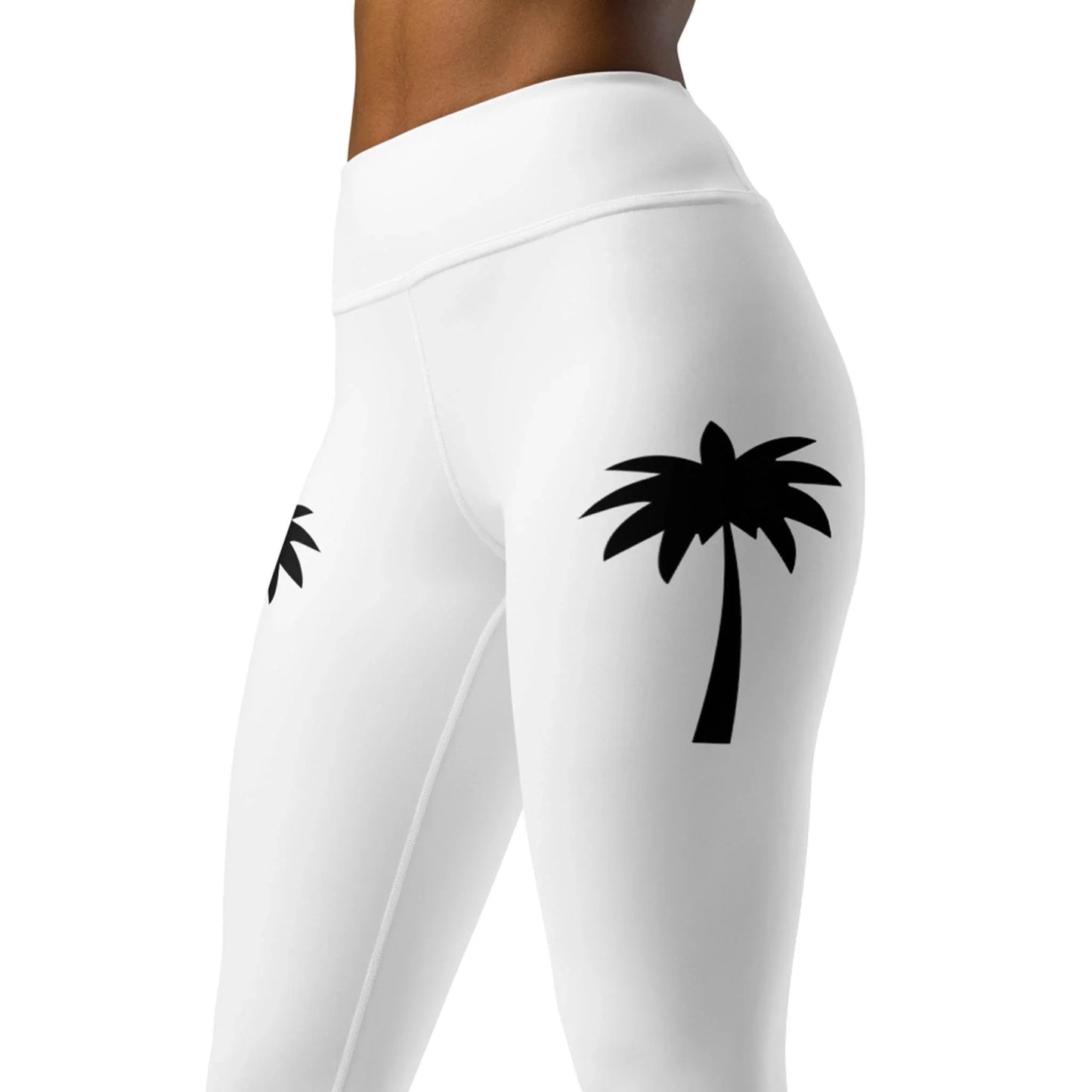 A person wears Printfuls Alpine High-Rise Yoga Leggings for women, featuring black palm tree silhouettes on white four-way stretch fabric. The athleisure leggings are shown from lower torso to upper legs.