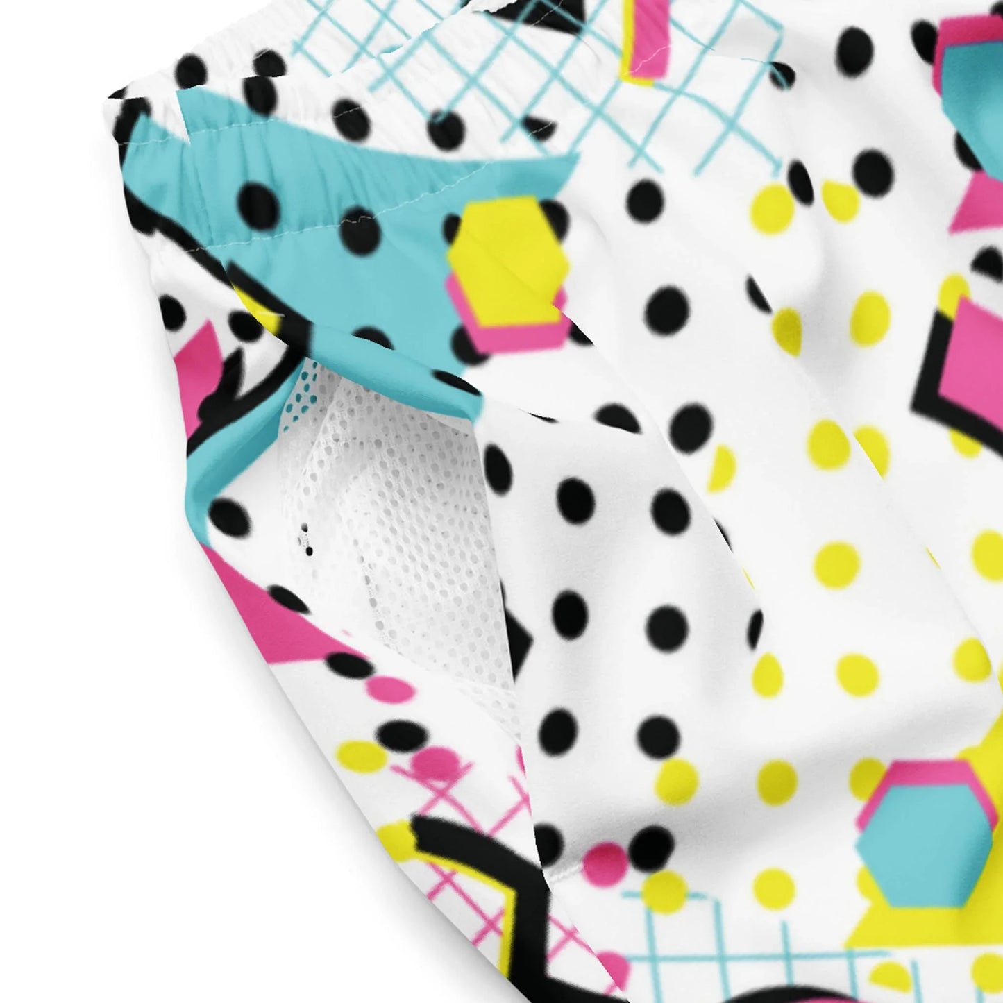 Close-up of colorful Mambí fabric with a retro geometric pattern featuring black dots, yellow spots, teal shapes, pink hexagons, and light blue grid lines on a white background; mesh lining is visible inside.