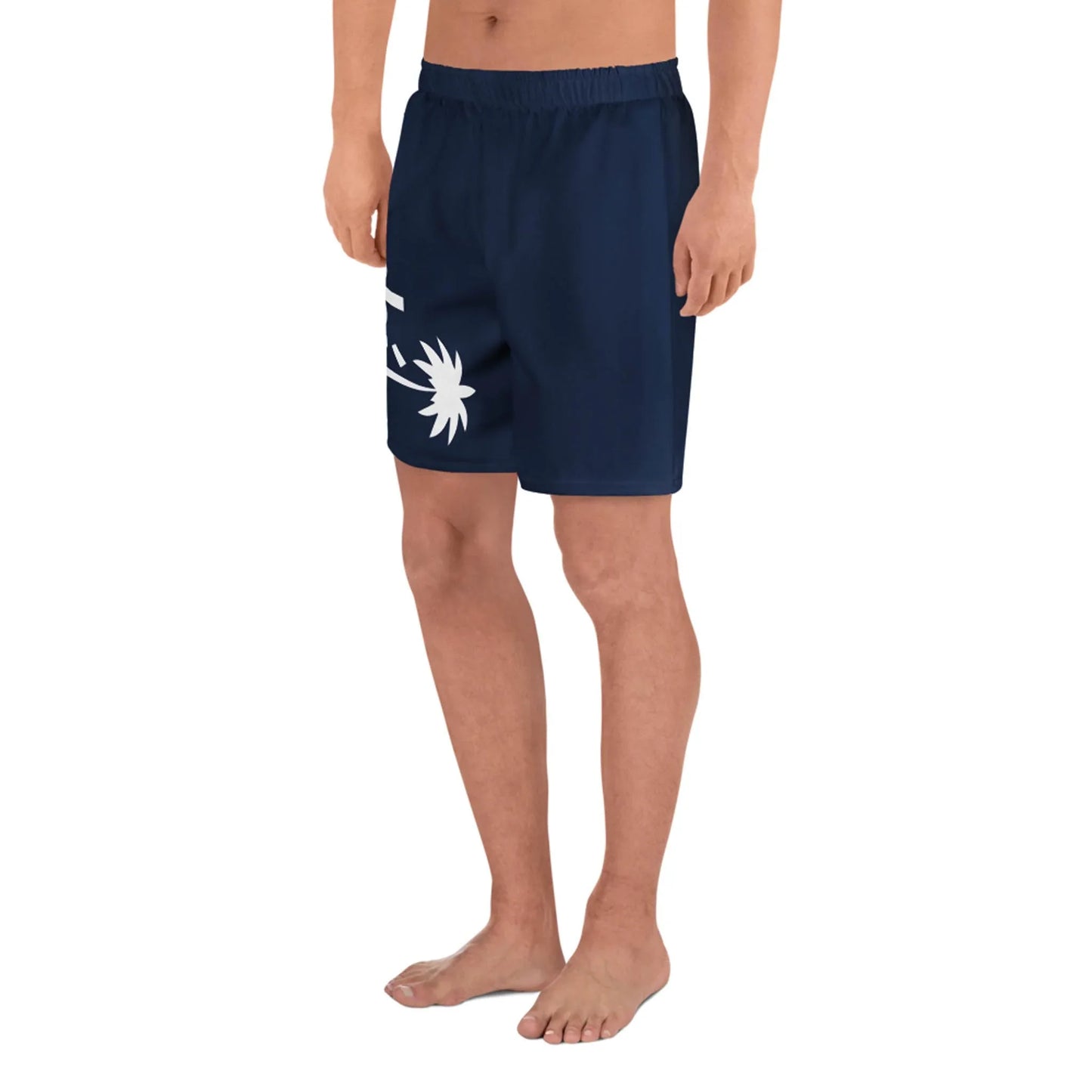 A person stands barefoot wearing Printful Belmar Long Athletic Shorts | Unisex in navy blue with a white graphic on the left leg. Designed for running, these shorts have an elastic waistband for comfort and performance against a plain background.