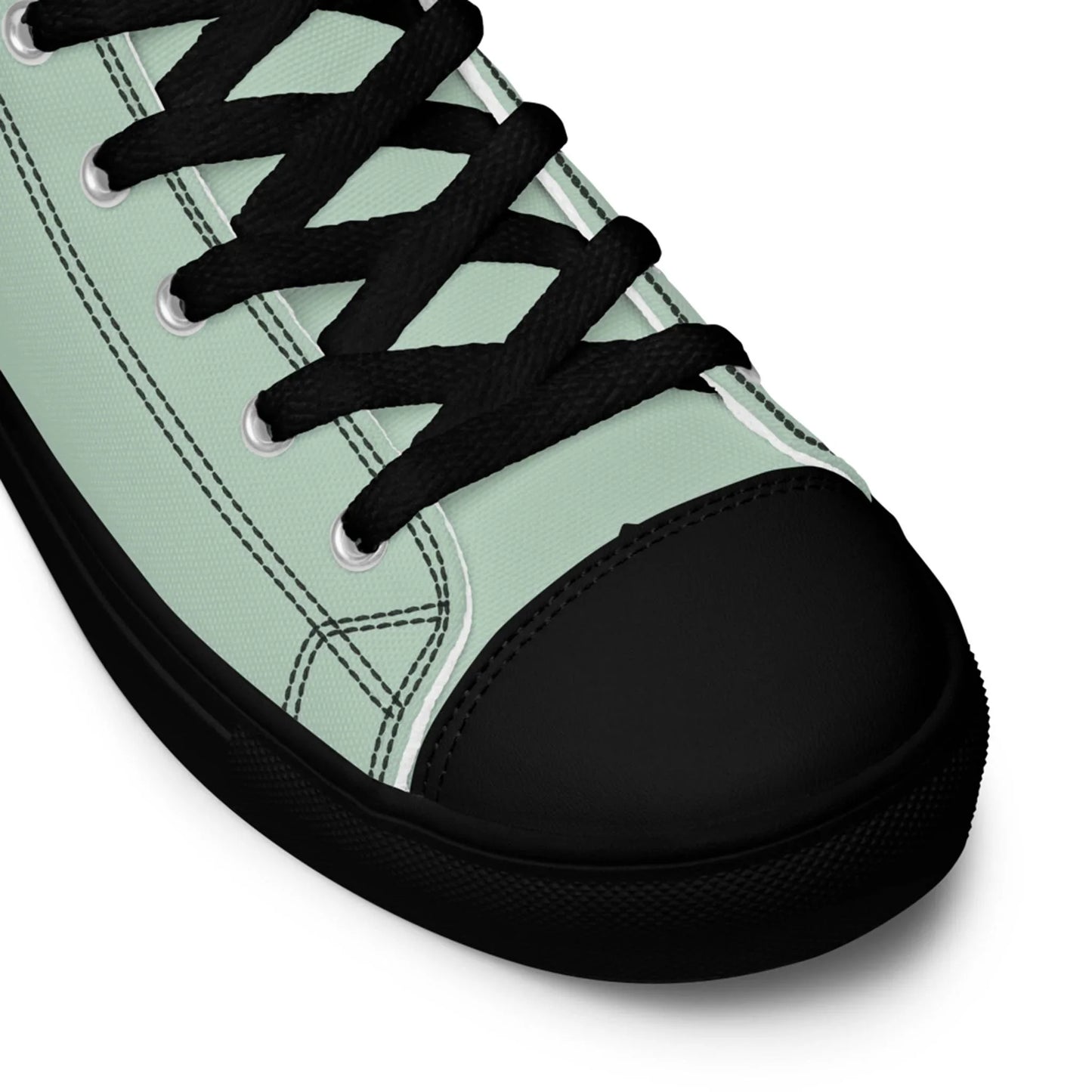 A close-up view of a light green Mambí canvas sneaker with black laces, black rubber toe cap, and black sole, showing detailed stitching and eyelets.