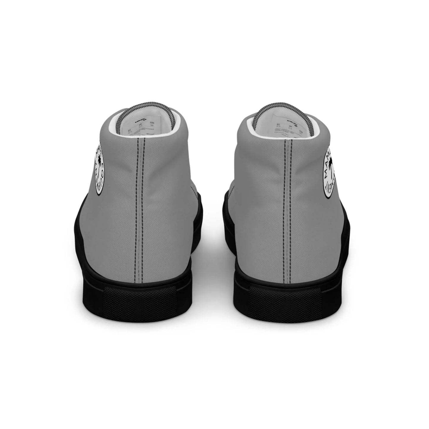 A pair of light gray Mambí high-top sneakers with black soles, shown from the back. Each shoe features a circular black and white logo on the heel.