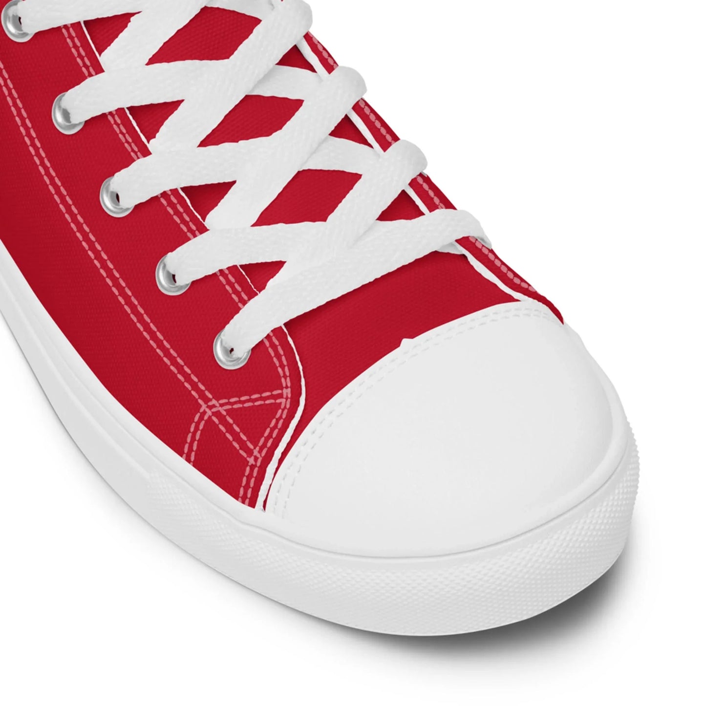 Close-up of the toe and laces of a red Mambí canvas sneaker with white stitching, white rubber toe cap, and white laces against a plain background.
