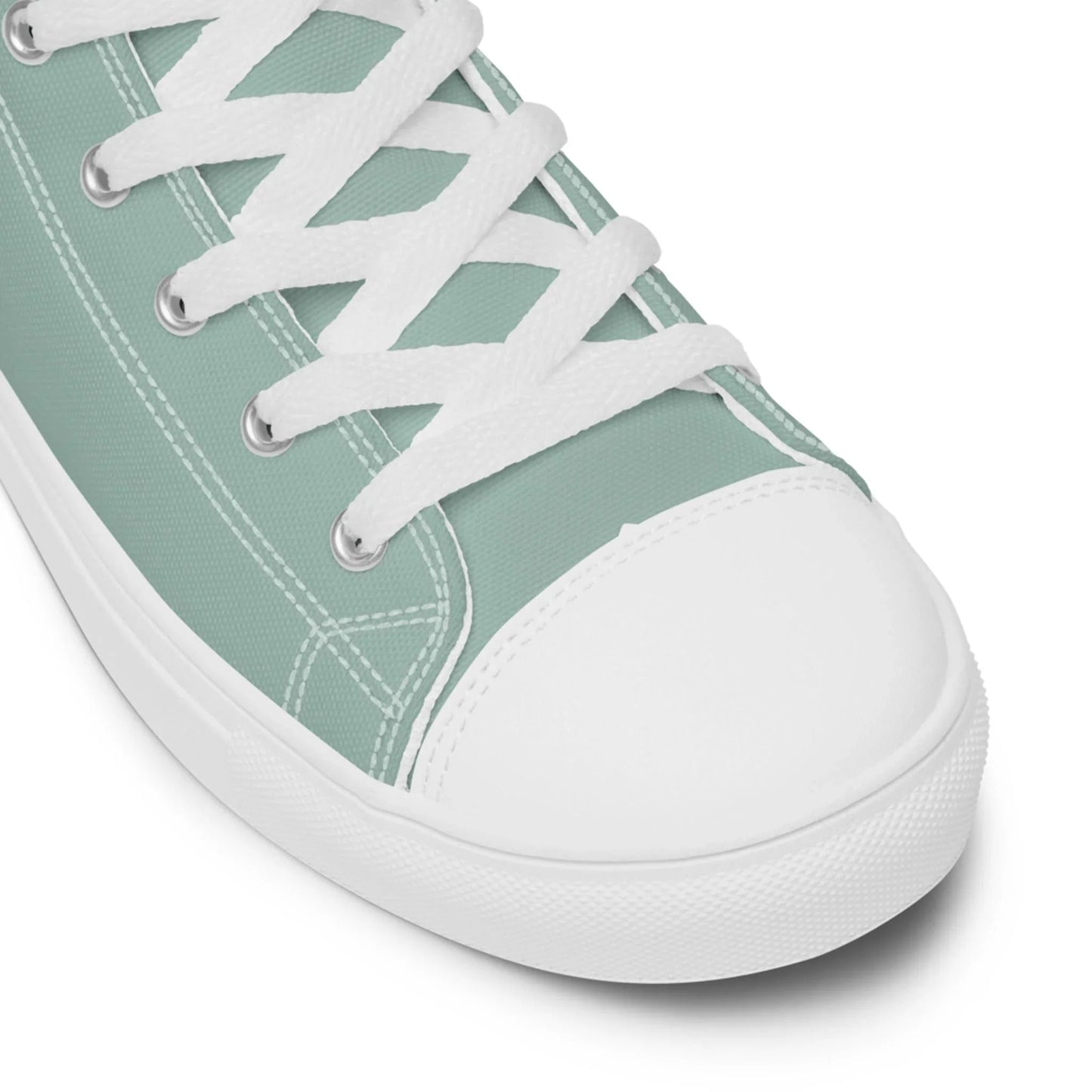 Close-up of a light green Mambí canvas sneaker with white laces, white stitching, and a white rubber toe cap and sole. The shoe is angled to show both the side and top view.