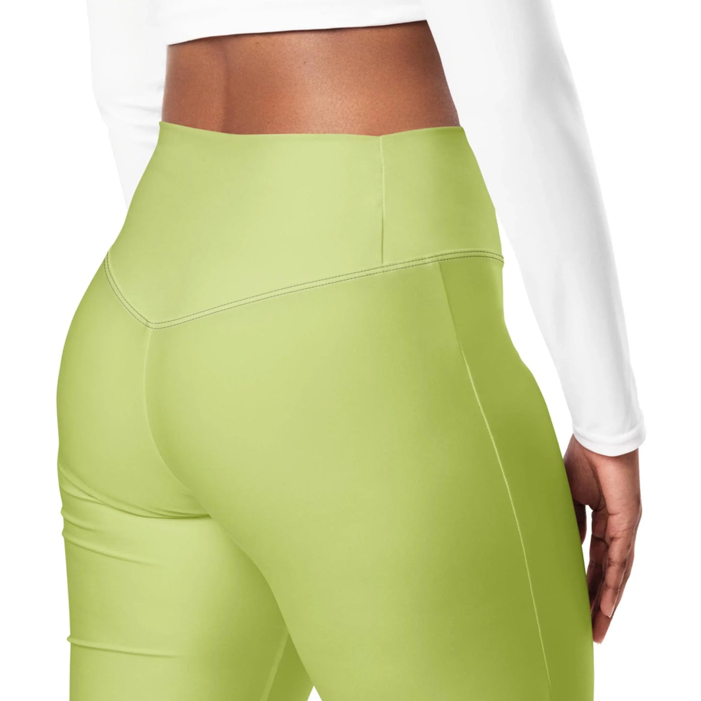 A woman is shown from the back and waist down, modeling Printful’s Carolina Flared Performance Leggings for women in high-waist light green, paired with a long-sleeve white crop top against a white background.