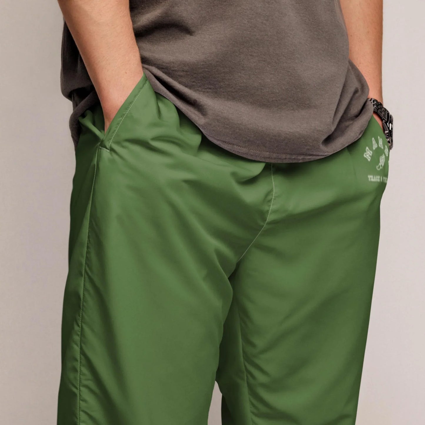 A person wearing a gray Mambí t-shirt and green athletic shorts with hands in the pockets, shown from waist to mid-thigh.