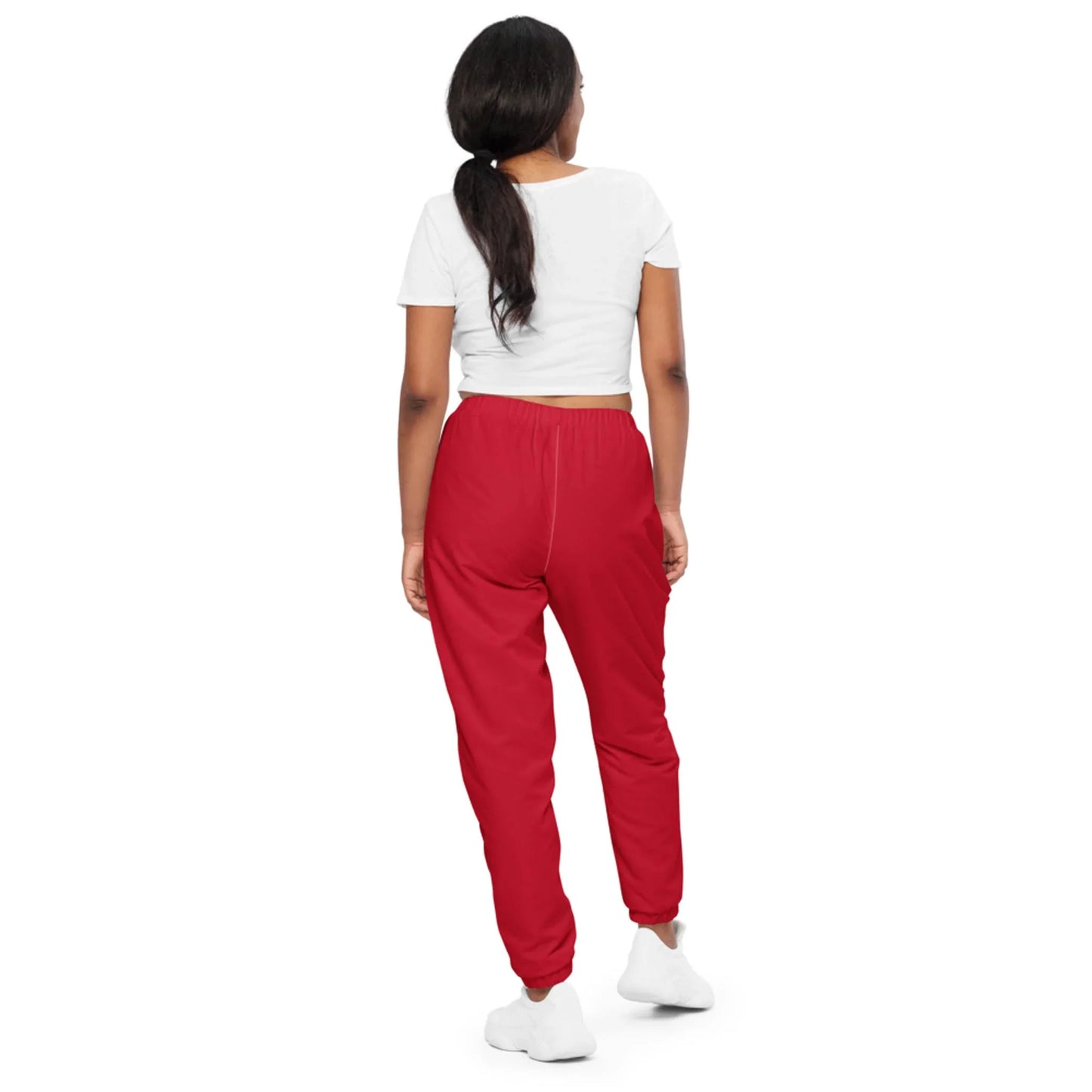 A woman stands facing away, wearing a white Mambí cropped t-shirt, red jogger pants, and white sneakers. Her dark hair is tied back in a low ponytail against a plain white background.