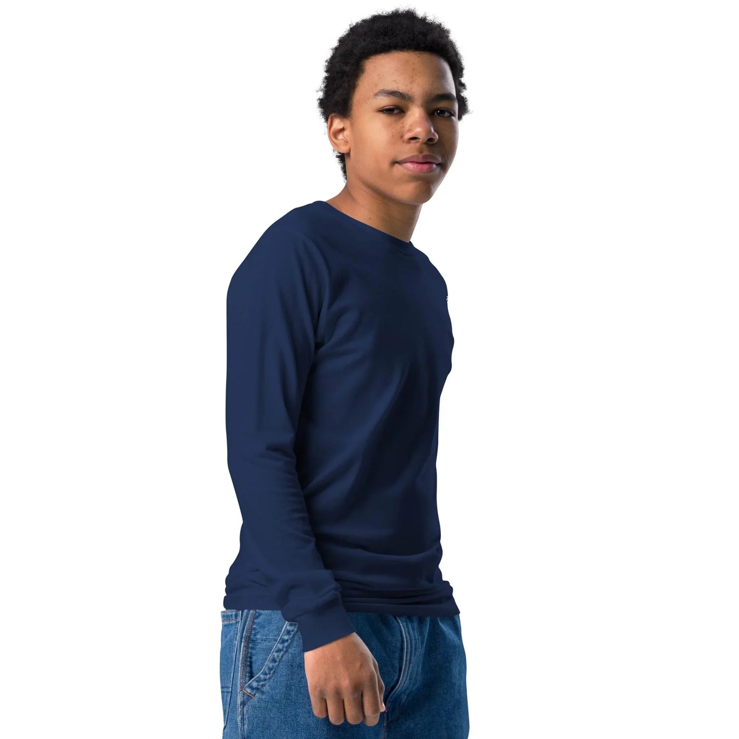 A young person with short curly hair wears a navy blue long-sleeve shirt and blue jeans, standing against a plain white background. They embody the modern spirit of a Mambí, looking slightly to the side with a neutral expression.