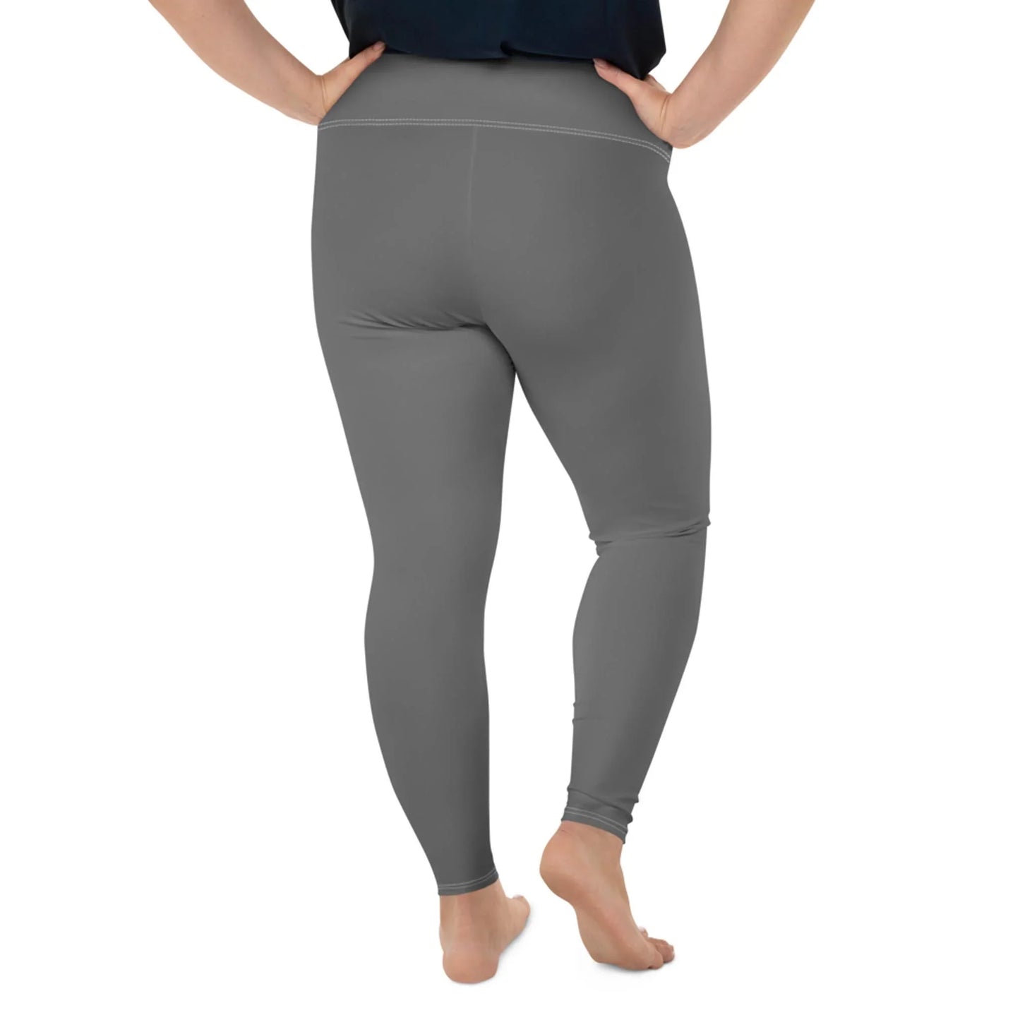 A person stands barefoot with hands on hips, wearing high-waisted, gray Mambí leggings and a black top. The image is taken from behind, showing the full length of the leggings.