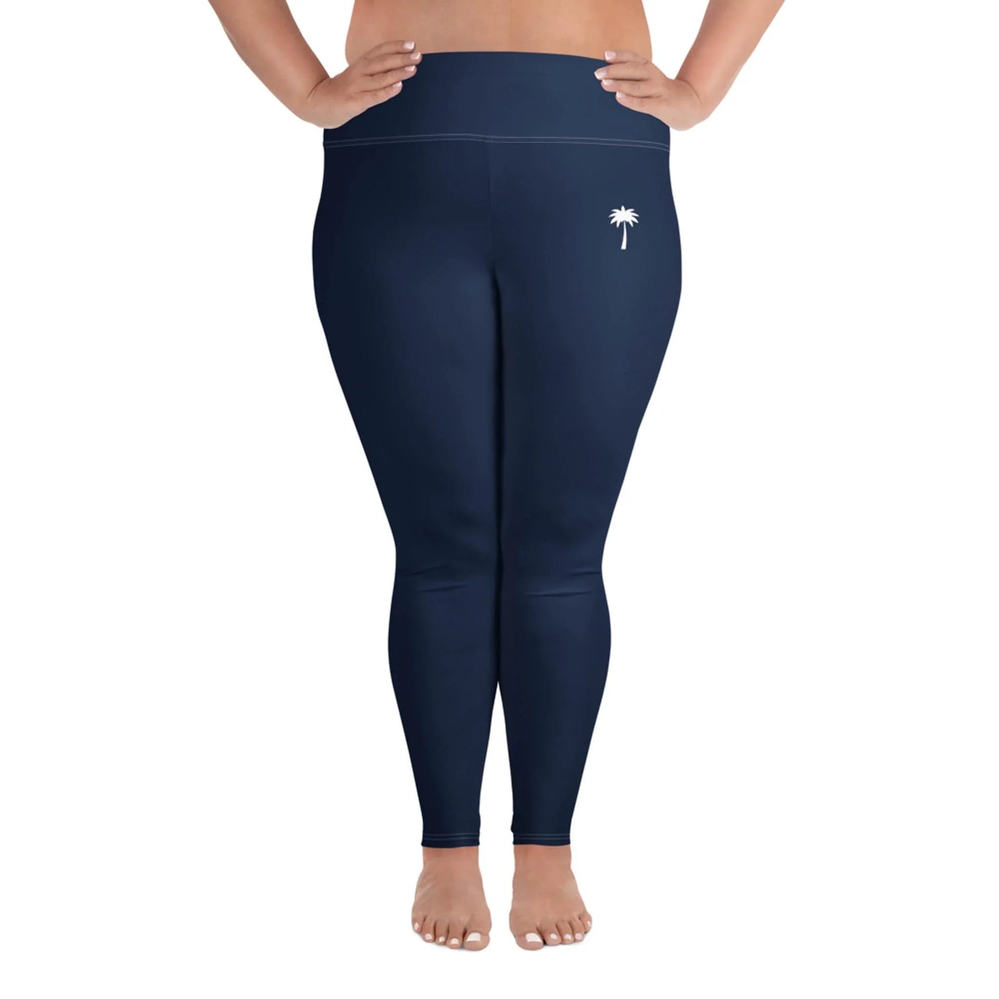 A person stands barefoot, wearing high-waisted, navy blue Mambí leggings with a small white palm tree design on the left hip, against a white background.