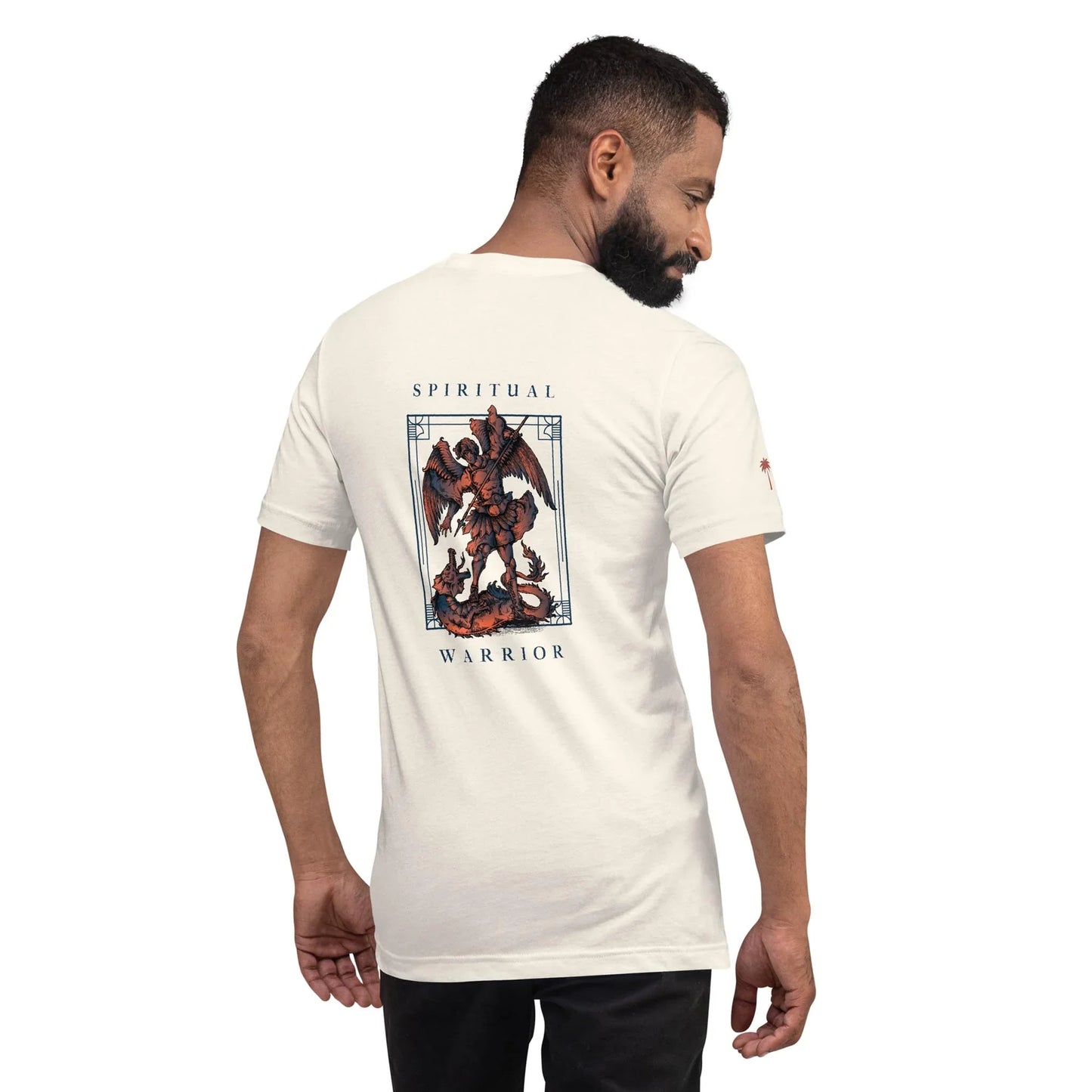A man with short hair and a beard wears a white T-shirt. On the back, there’s an illustration of an armored Mambí warrior fighting a dragon, framed by the words Spiritual Warrior. The man is looking over his shoulder.