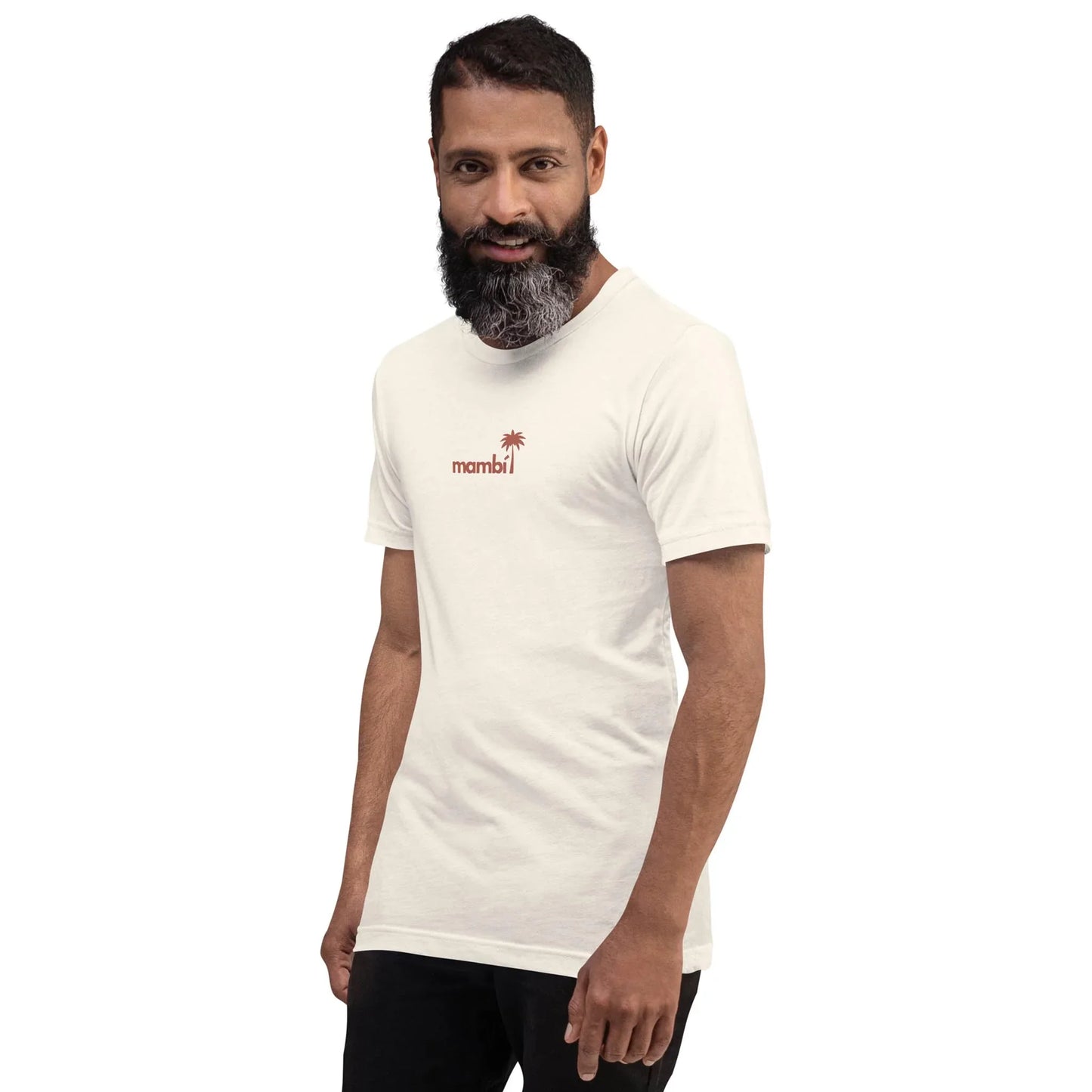 A man with a beard and mustache is wearing a white t-shirt with Mambí and a small red palm tree graphic. He is smiling and standing against a plain white background.