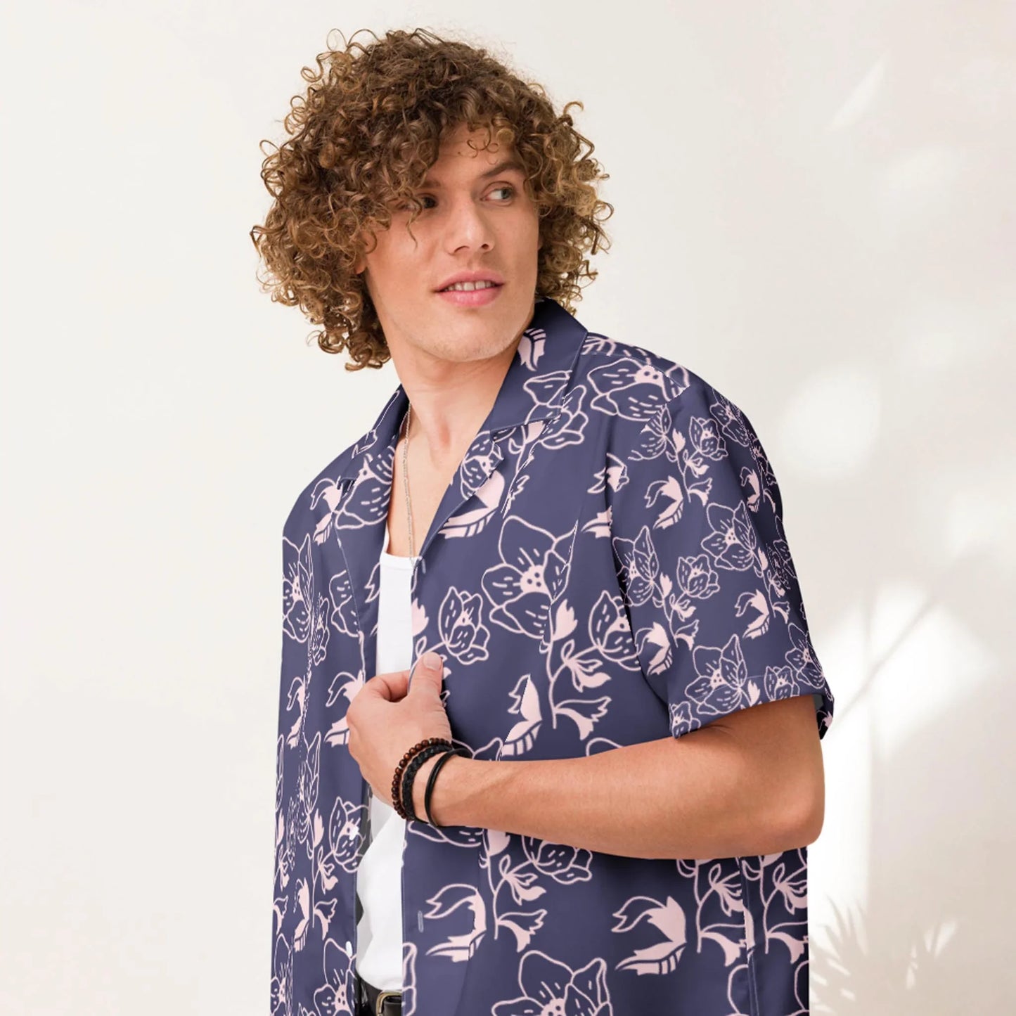 A person with curly hair wearing a navy blue Mambí shirt with a pink floral pattern over a white top, looking to the side against a light-colored background.