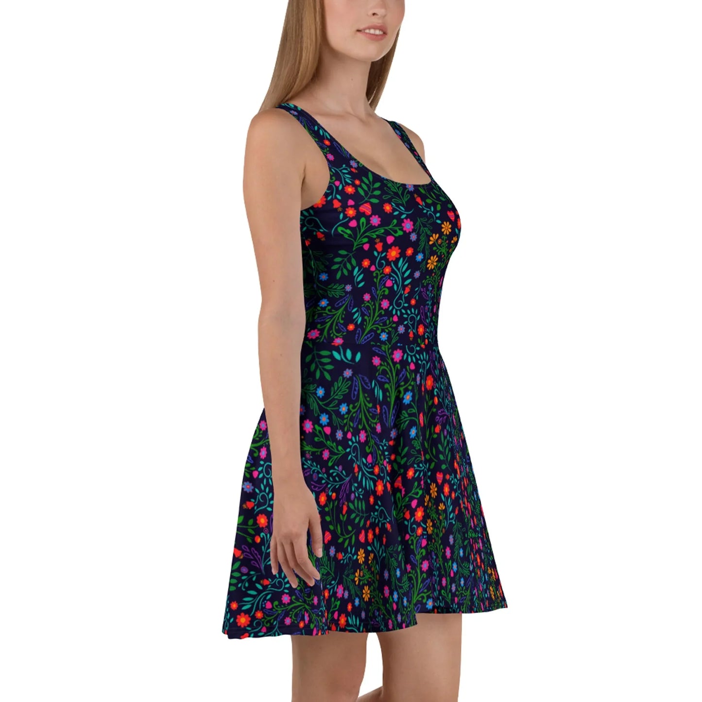 A woman wears the Printful Coco Skater Dress, featuring a flared skirt and vibrant floral pattern on a dark background. Made from soft fabric, she stands sideways with her head slightly turned and arms relaxed.