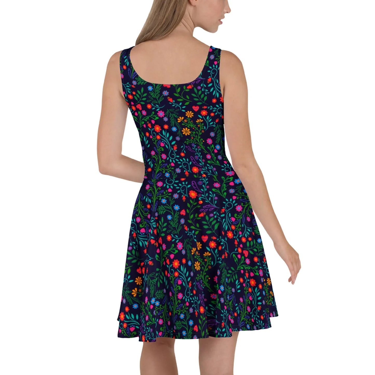 A woman models the Printful Coco Skater Dress, featuring a flared skirt and sleeveless design. The soft fabric showcases bright floral and green leaf patterns on a dark background as she turns her head to the side.