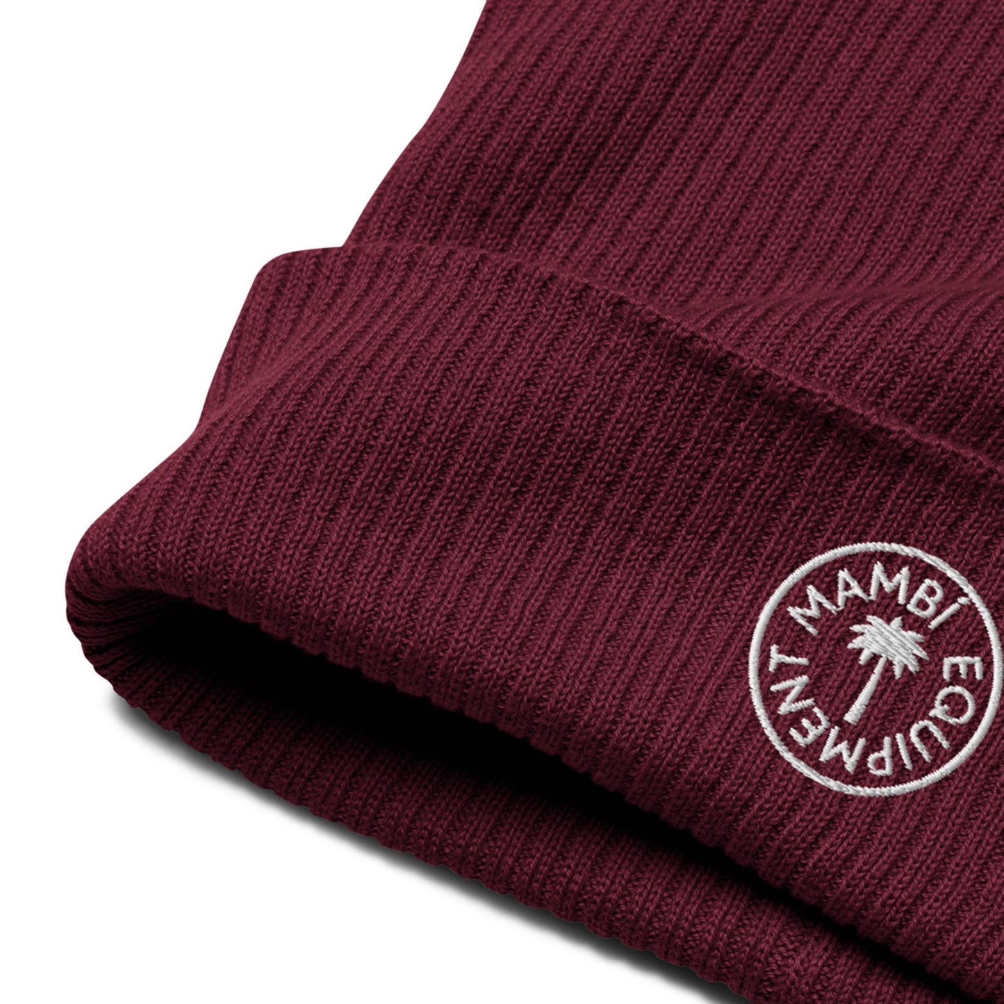 Close-up of a maroon ribbed knit beanie with a folded brim, featuring a white embroidered circular Mambí logo and palm tree design in the center.