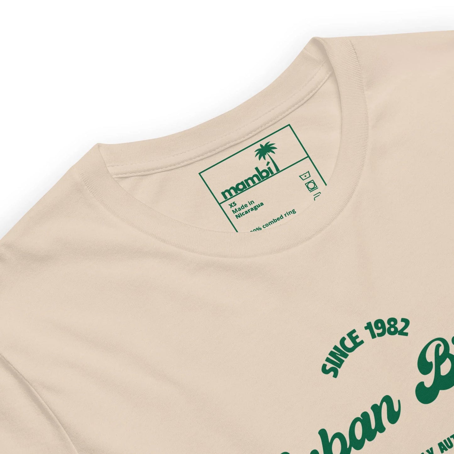A close-up of the Cuban Bros Graphic Tee from Printful, a beige unisex t-shirt with green chest text and an inner collar label showing a palm tree, Printful branding, size XL, and washing instructions.