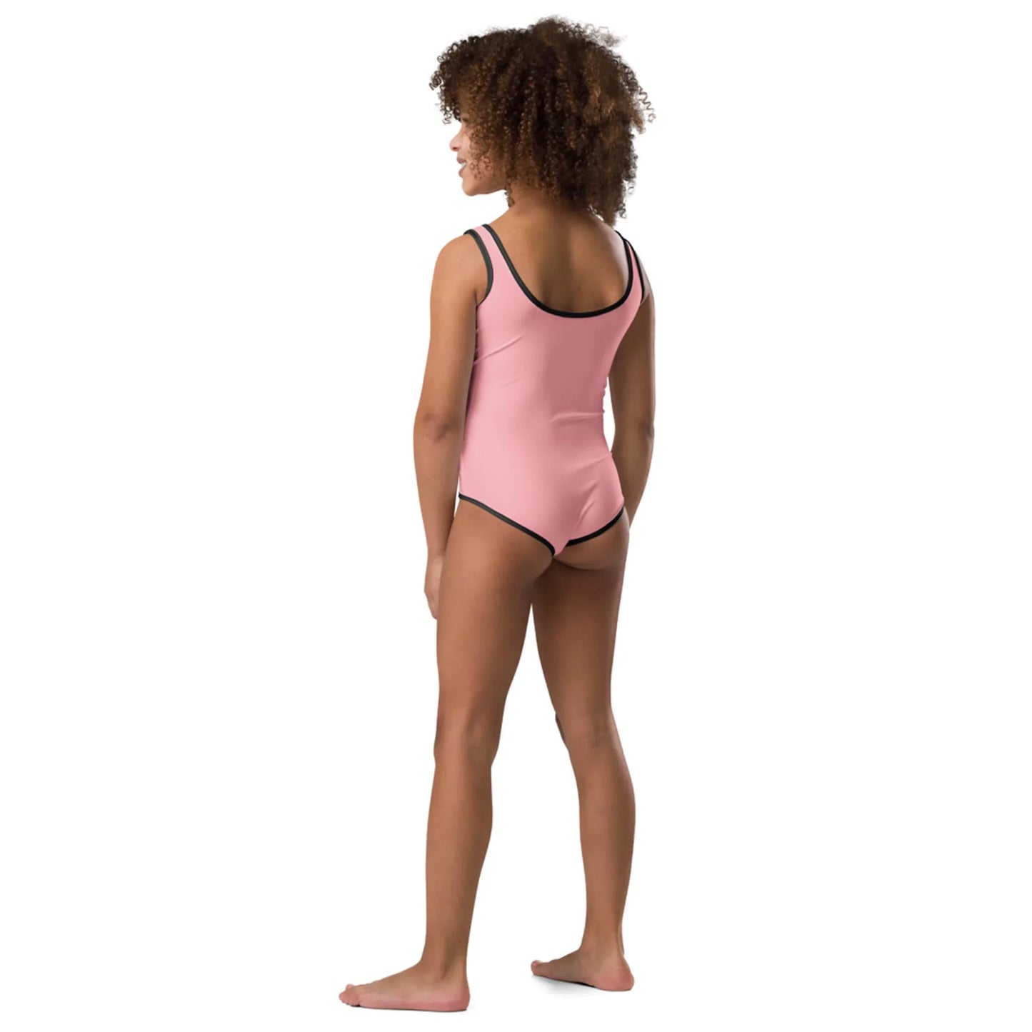 A young girl with curly hair stands barefoot, facing away, wearing the Daisy Classic One-Piece Swimsuit by Printful for toddlers & little kids, featuring vibrant prints and black trim, set against a plain white background.
