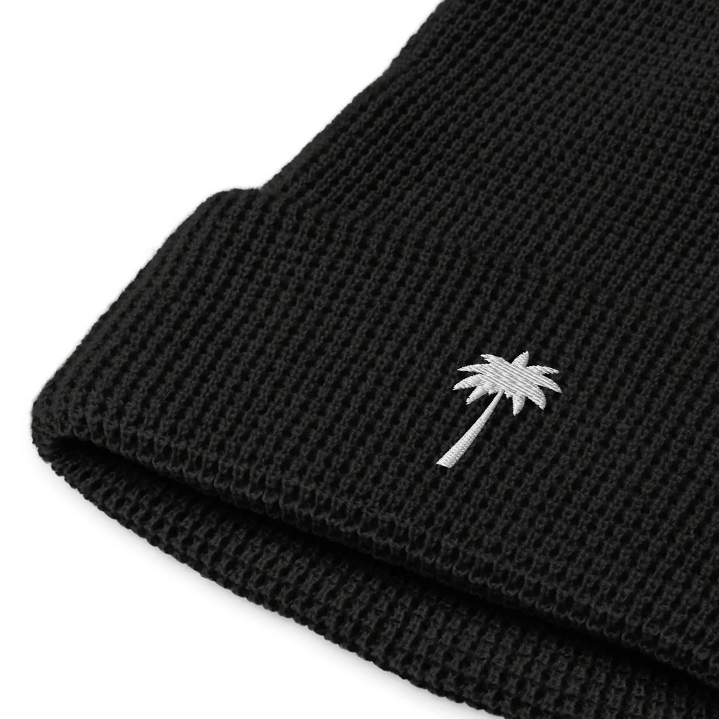 Close-up of a black knitted Mambí beanie featuring a small white palm tree embroidered on the folded cuff.
