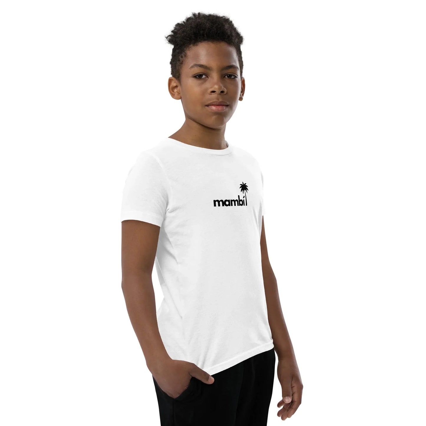 A young boy with short curly hair wears a white t-shirt featuring a small black palm tree and the word Mambí on the chest. He stands sideways, one hand in his pocket, looking confidently at the camera.