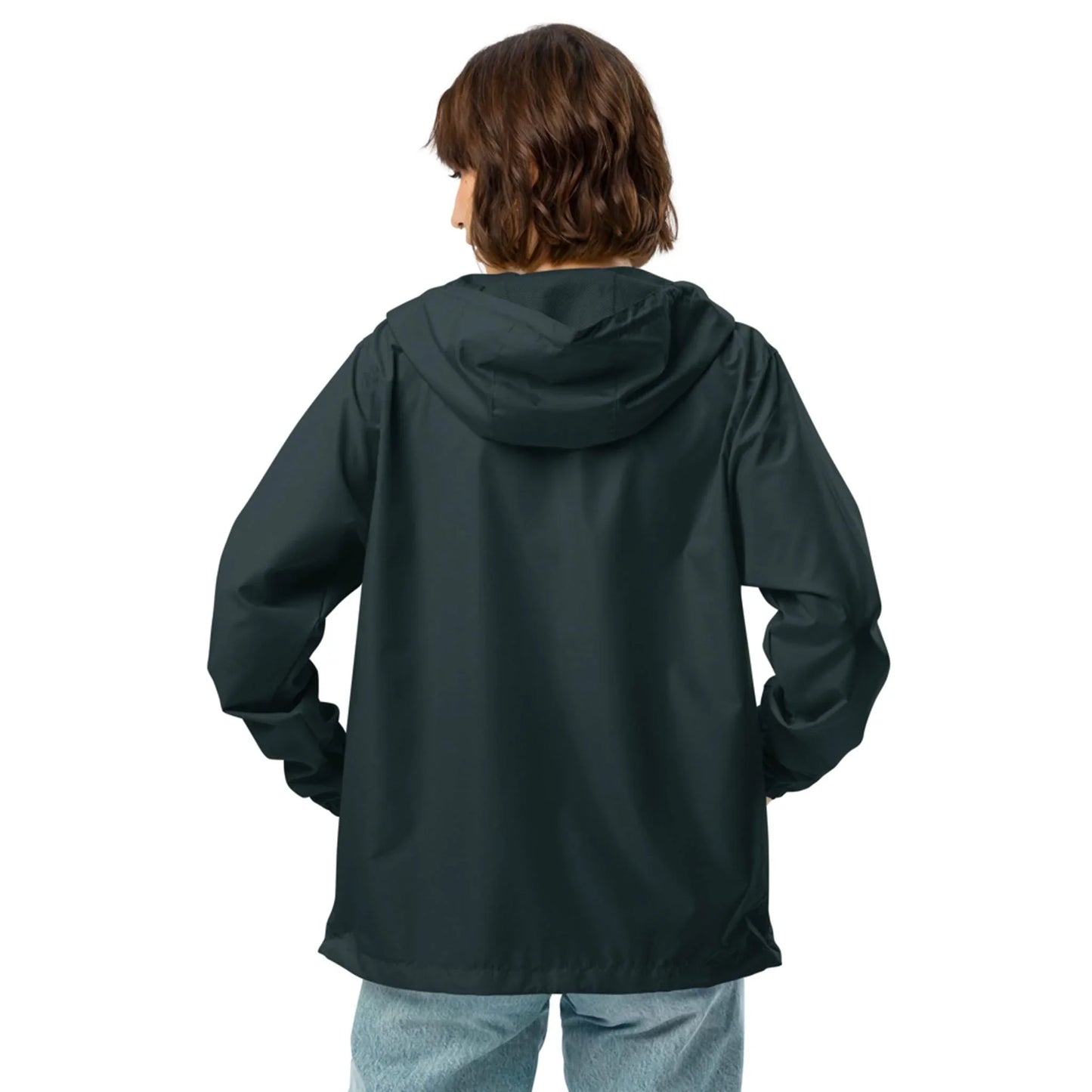 A person with short brown hair, wearing a dark Mambí hooded jacket and light blue jeans, stands with their back to the camera against a plain white background.