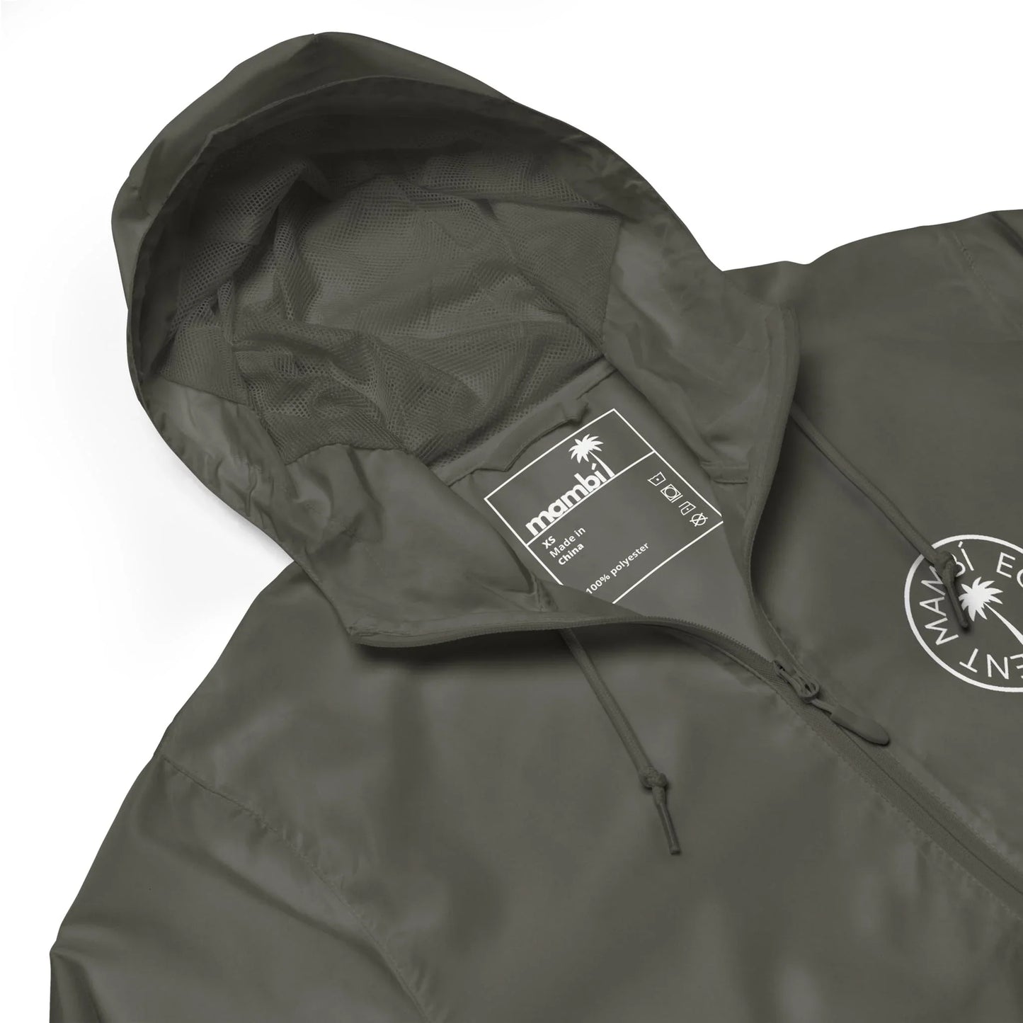 A close-up of an olive green hooded jacket with a drawstring hood. The label inside reads “manahil” with size and care details. A circular Mambí logo featuring text and a palm tree decorates the chest.
