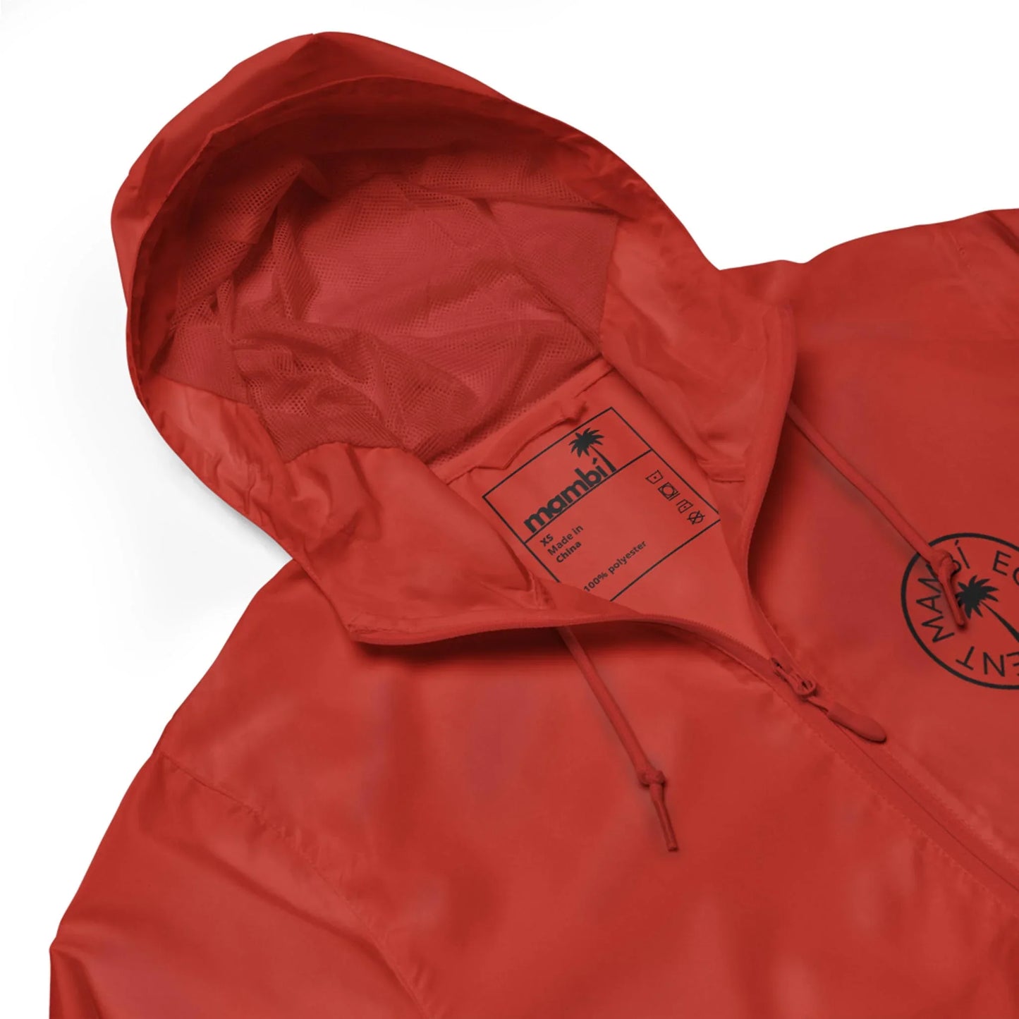 A close-up of a red hooded jacket featuring a black circular logo on the chest and a label inside the hood that reads Mambí with care instructions.