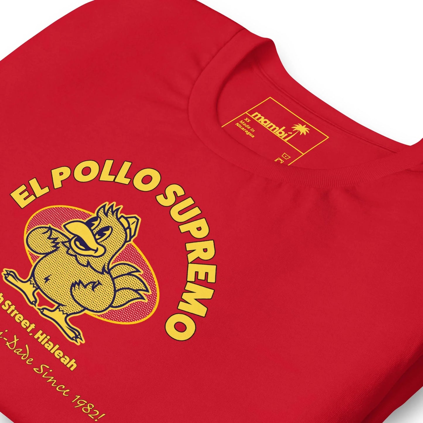 A red T-shirt features a cartoon chicken flexing its muscles with the text EL POLLO SUPREMO above it. Below, it reads 8th Street, Hialeah and ¡Sabe Since 1982! The shirt tag displays authentic Mambí branding.