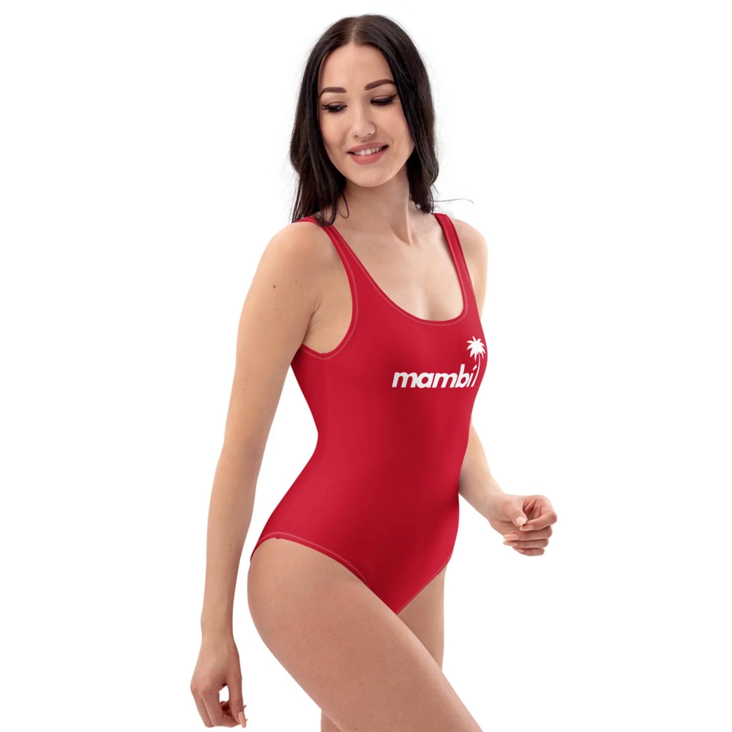 A woman with long dark hair wears a red one-piece swimsuit with Mambí and a small palm tree graphic on the front. She is smiling and looking to the side against a plain white background.