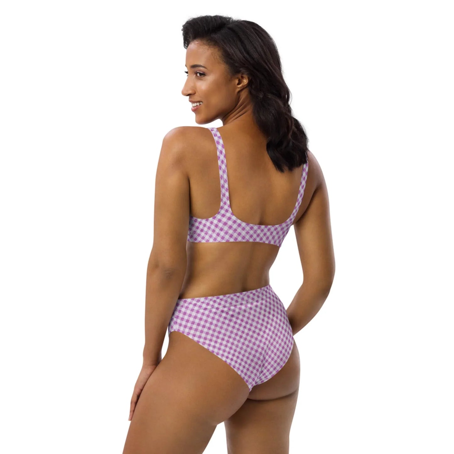 A woman stands turned to the side, looking over her shoulder with a smile, wearing a high-waisted, Mambí lavender and white checkered bikini against a plain white background.
