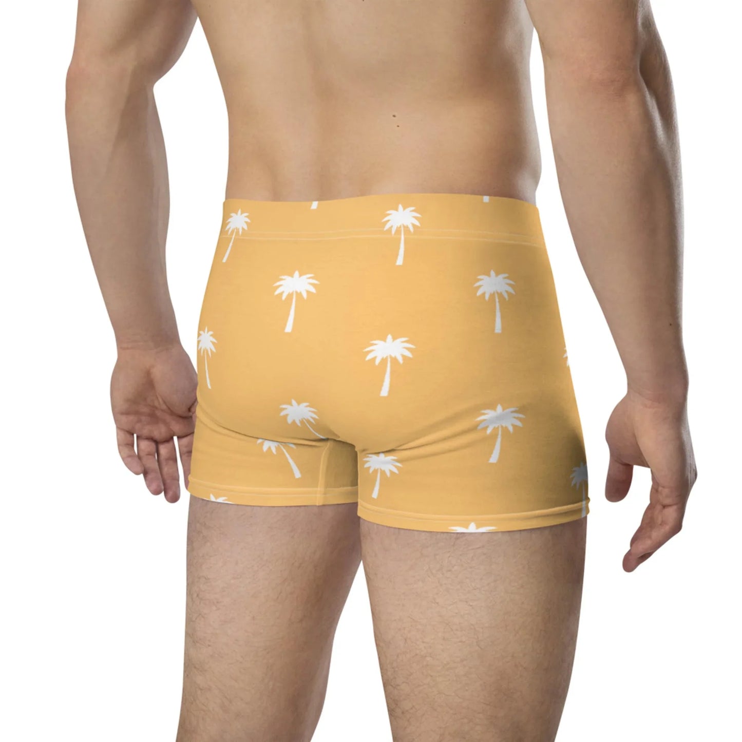 A man is seen from behind wearing Printful’s Emerson Boxer Briefs in yellow with a white palm tree print. The no-back-seam design ensures a seamless fit as he stands against a plain white background.