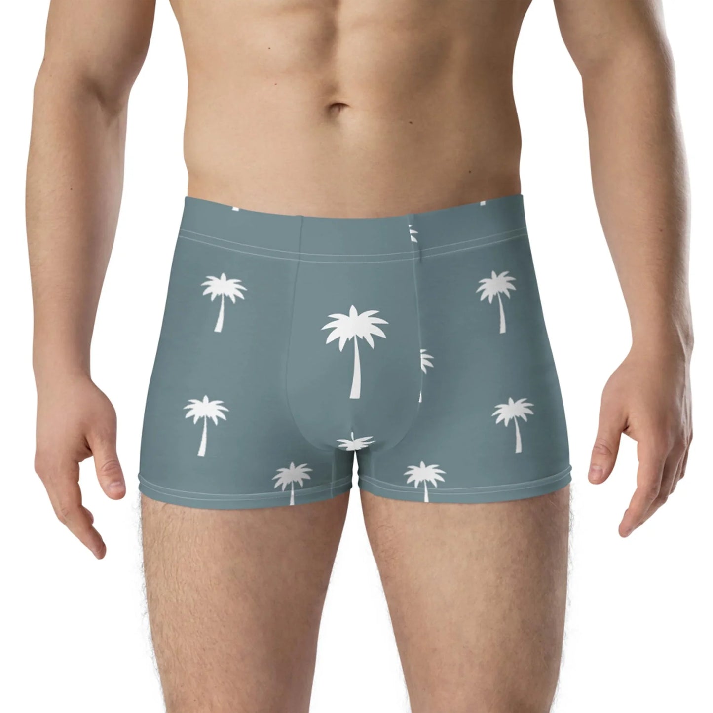 A man wears the Printful Emerson Boxer Brief for men, featuring a teal and white palm tree pattern and seamless fit, shown from mid-chest to upper thighs against a plain background.