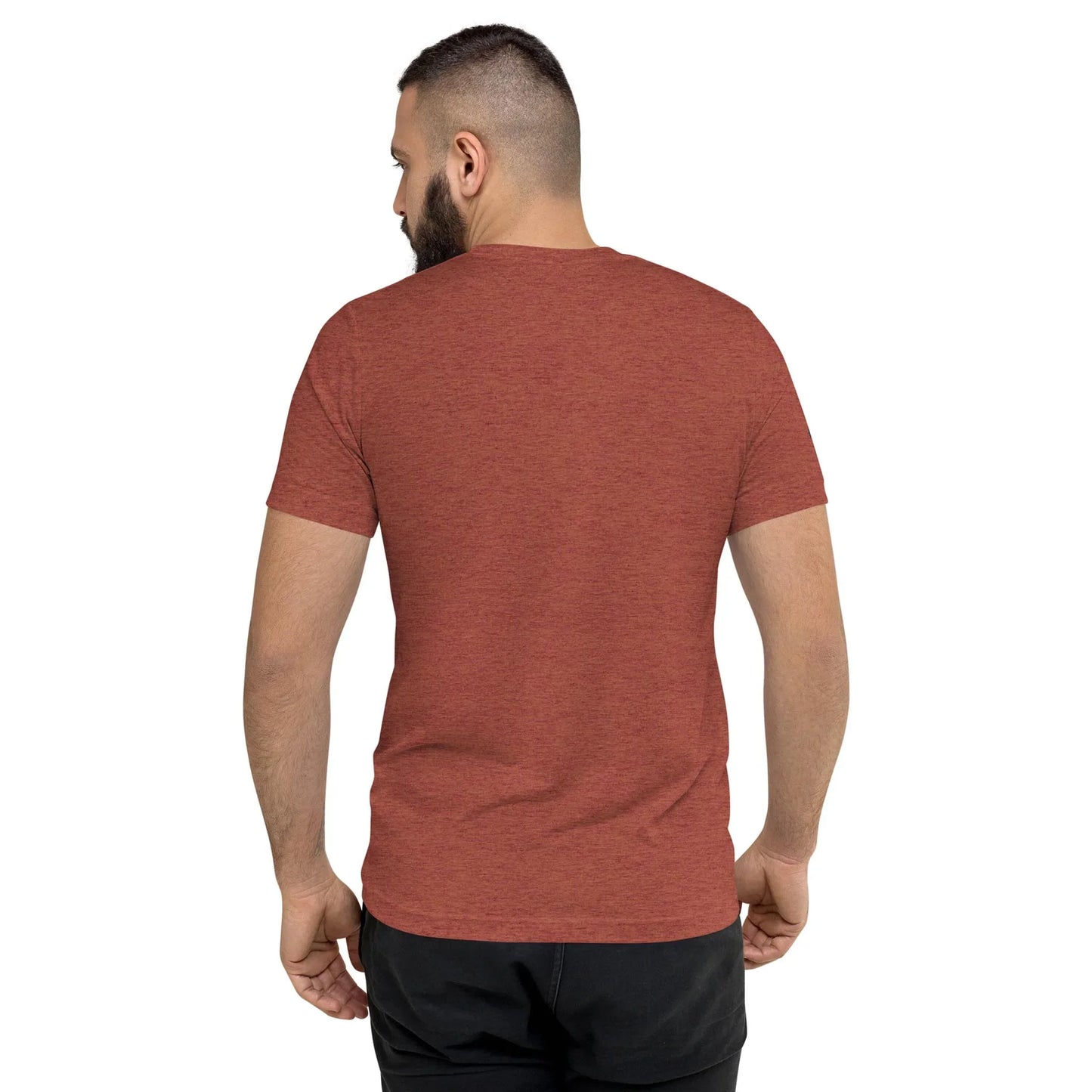 A man with short dark hair and a beard is seen from behind, wearing a red heathered Mambí short-sleeve t-shirt and black pants, standing against a plain white background.