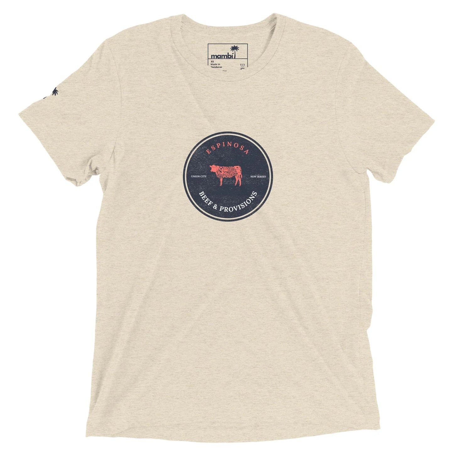 A light beige short-sleeve T-shirt featuring a round navy blue emblem with a red cow and the words Espinosa Beef & Provisions on the chest, inspired by Mambí spirit. A small logo tag accents the neck.