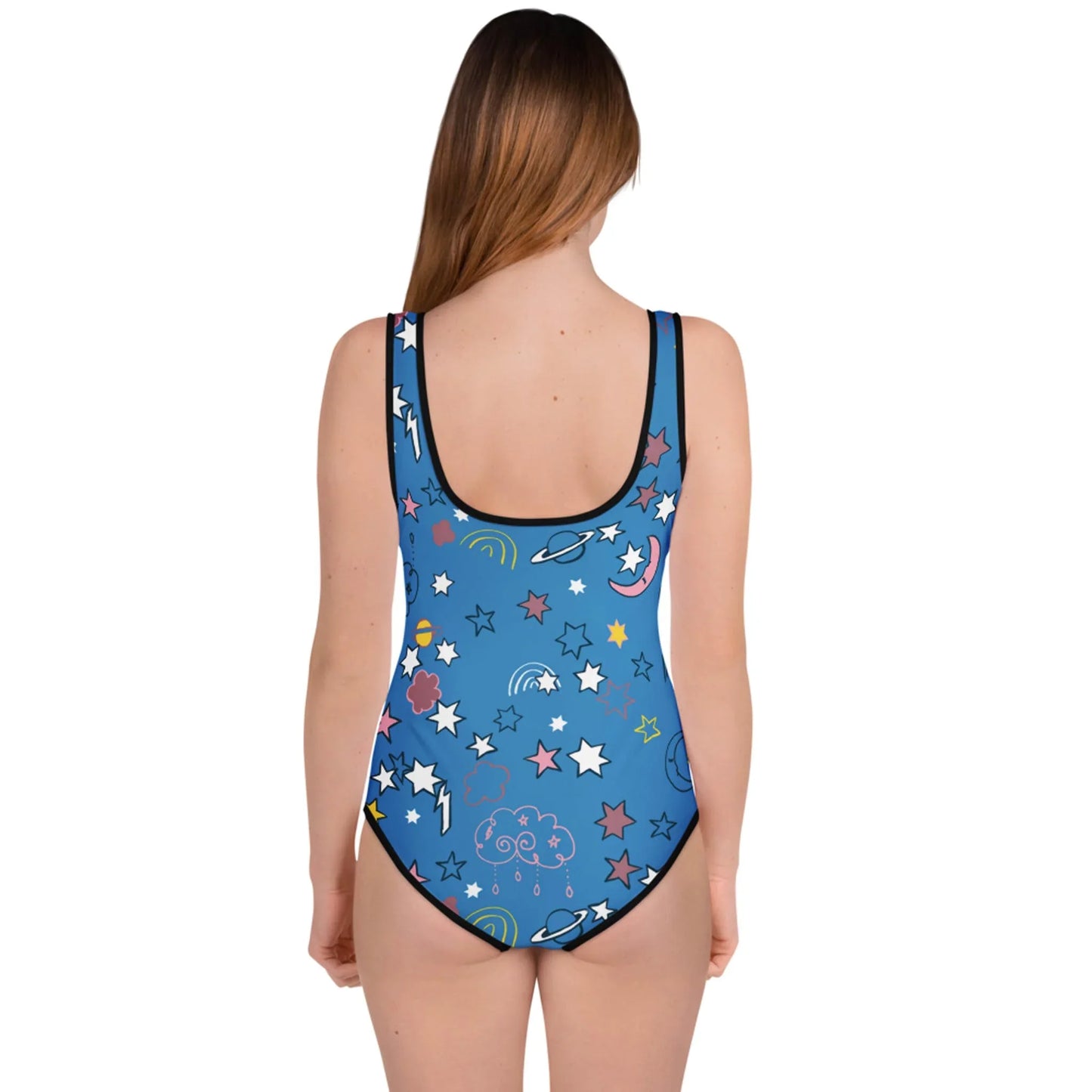 A woman with long brown hair faces away, wearing a blue Mambí one-piece swimsuit decorated with colorful stars, clouds, moons, planets, and rainbows. The background is plain white.