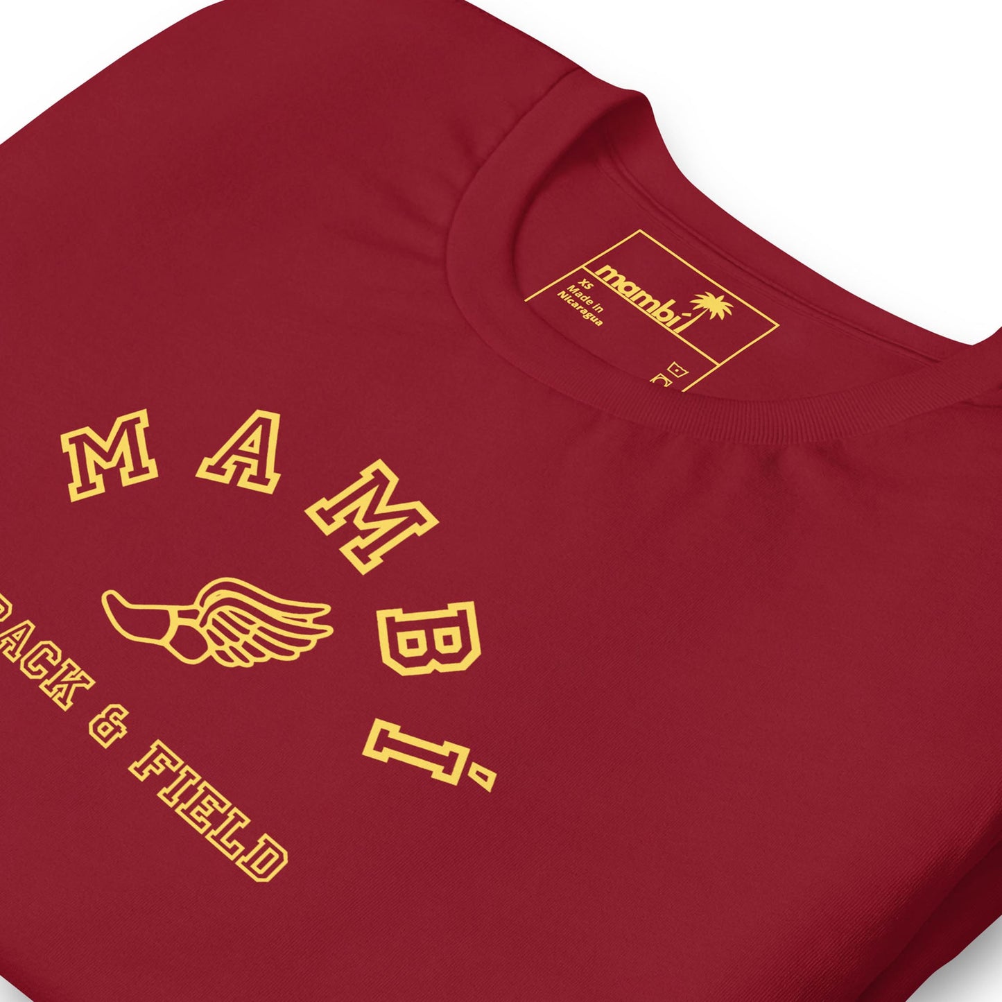A red t-shirt with yellow text that reads “Mambí” above a winged shoe illustration, and “TRACK & FIELD” below. The inner label features a palm tree logo and brand details.