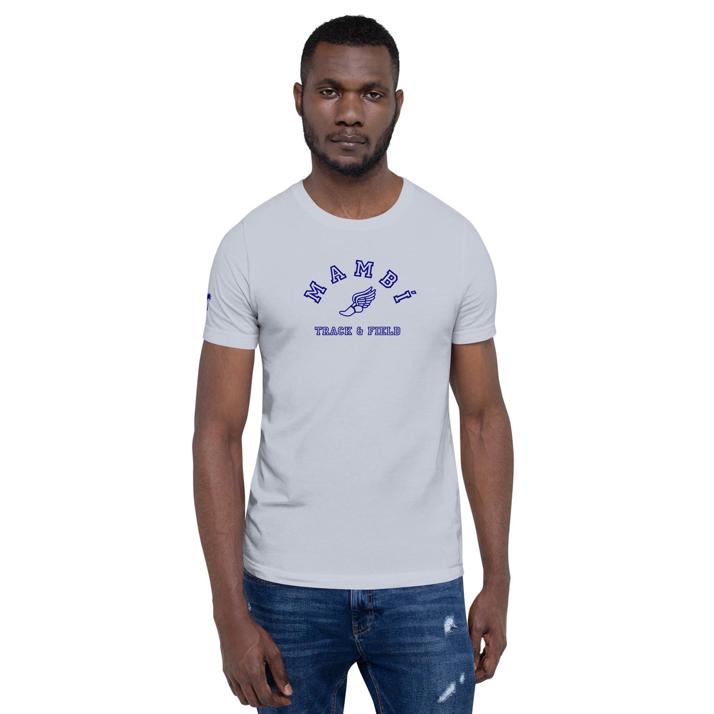 A man with a beard wears a light gray Mambí t-shirt that says NAMIBI TRACK & FIELD in blue text. He stands facing forward with a neutral expression and is also wearing slightly distressed blue jeans.