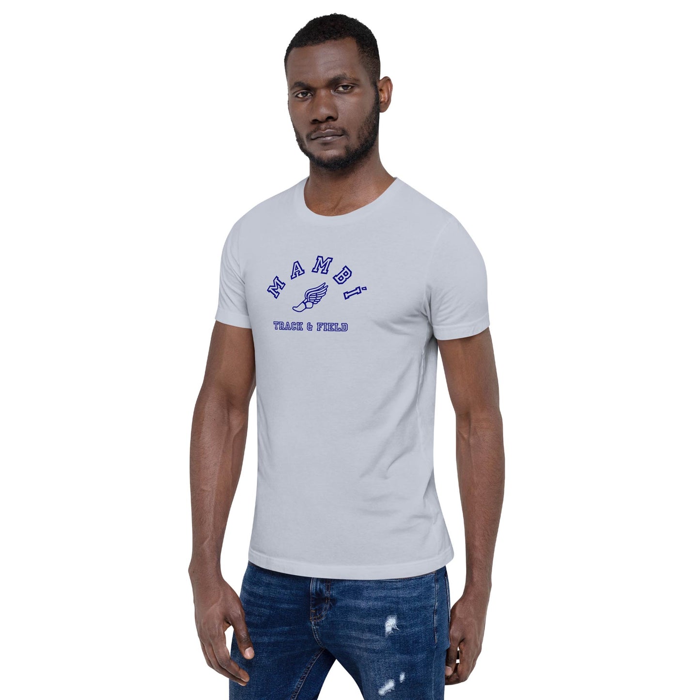 A man in a light gray Mambí t-shirt with blue text reading NAMDI TRACK & FIELD stands facing forward, one hand by his side and the other slightly bent, wearing ripped blue jeans.
