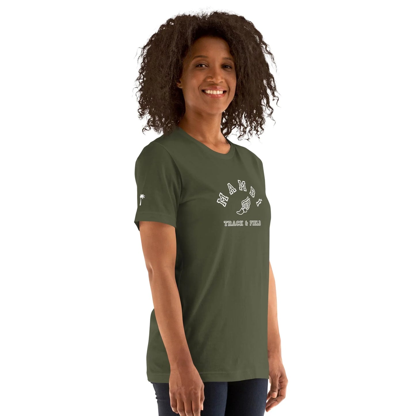 A woman with curly hair smiles while wearing a dark green Mambí T-shirt that reads “MADE IT” above a graphic of a raised hand and the words “PEACE & FUN” below. She stands against a plain white background.