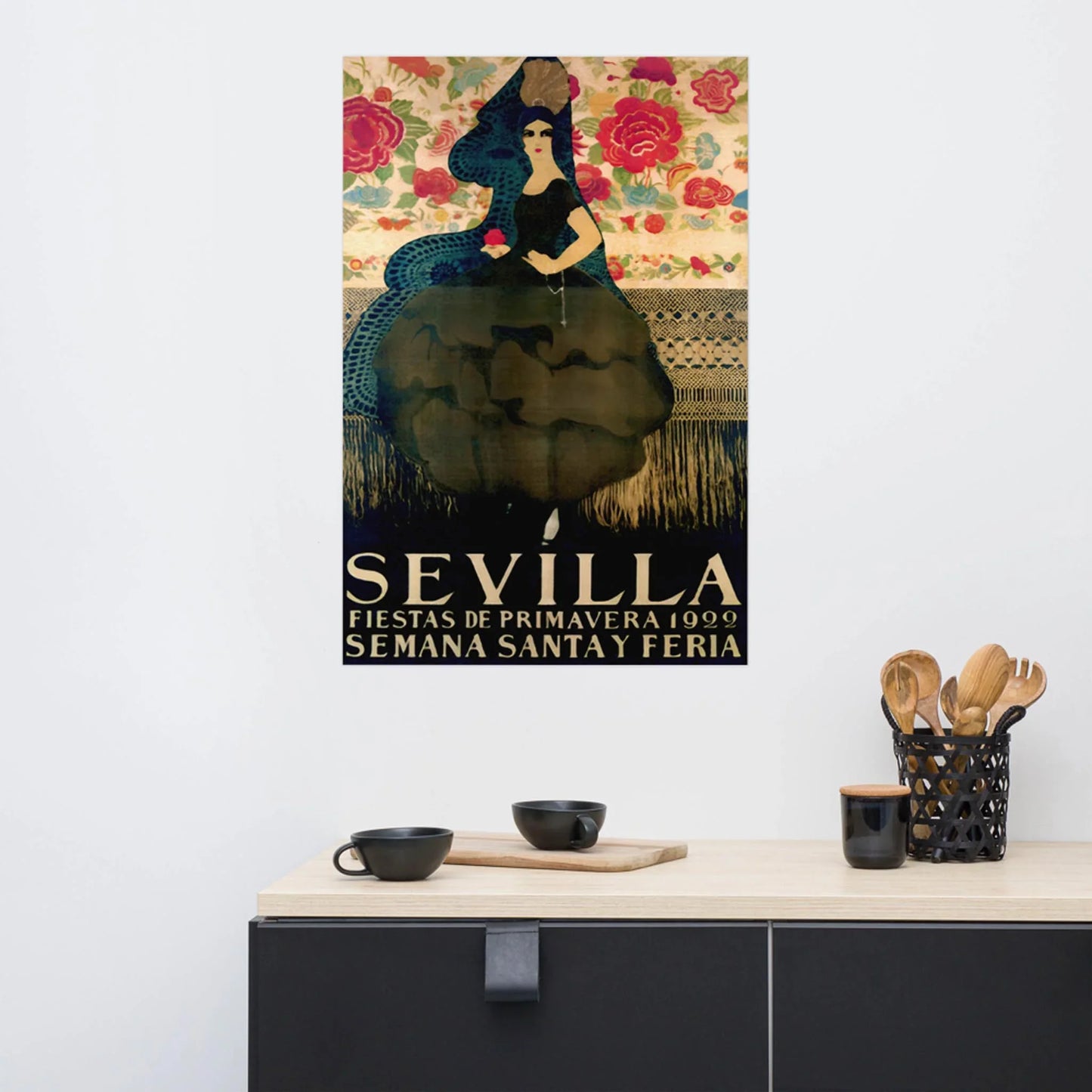 A colorful vintage Mambí poster on a white wall features a woman in a black dress and veil holding a rose, with floral patterns and the text “Sevilla Fiestas de Primavera 1930 Semana Santa y Feria” below. A countertop holds cups and utensils.