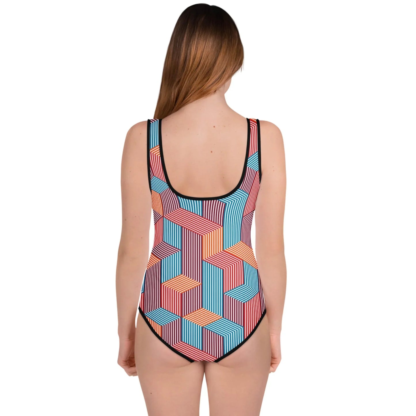 A woman with long brown hair stands facing away, wearing a Mambí one-piece swimsuit adorned with a colorful geometric pattern of interlocking striped shapes in blue, red, orange, and white.