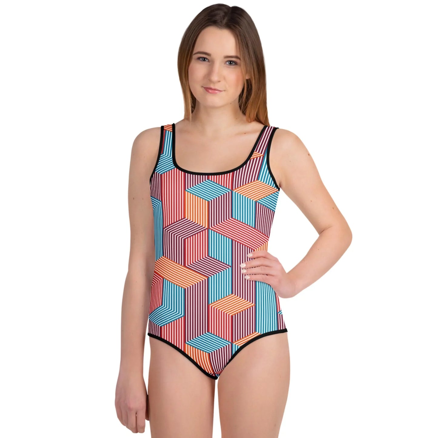 A young woman with straight brown hair wears a colorful, geometric-patterned Mambí one-piece swimsuit. She stands facing forward with one hand on her hip, smiling slightly against a white background.