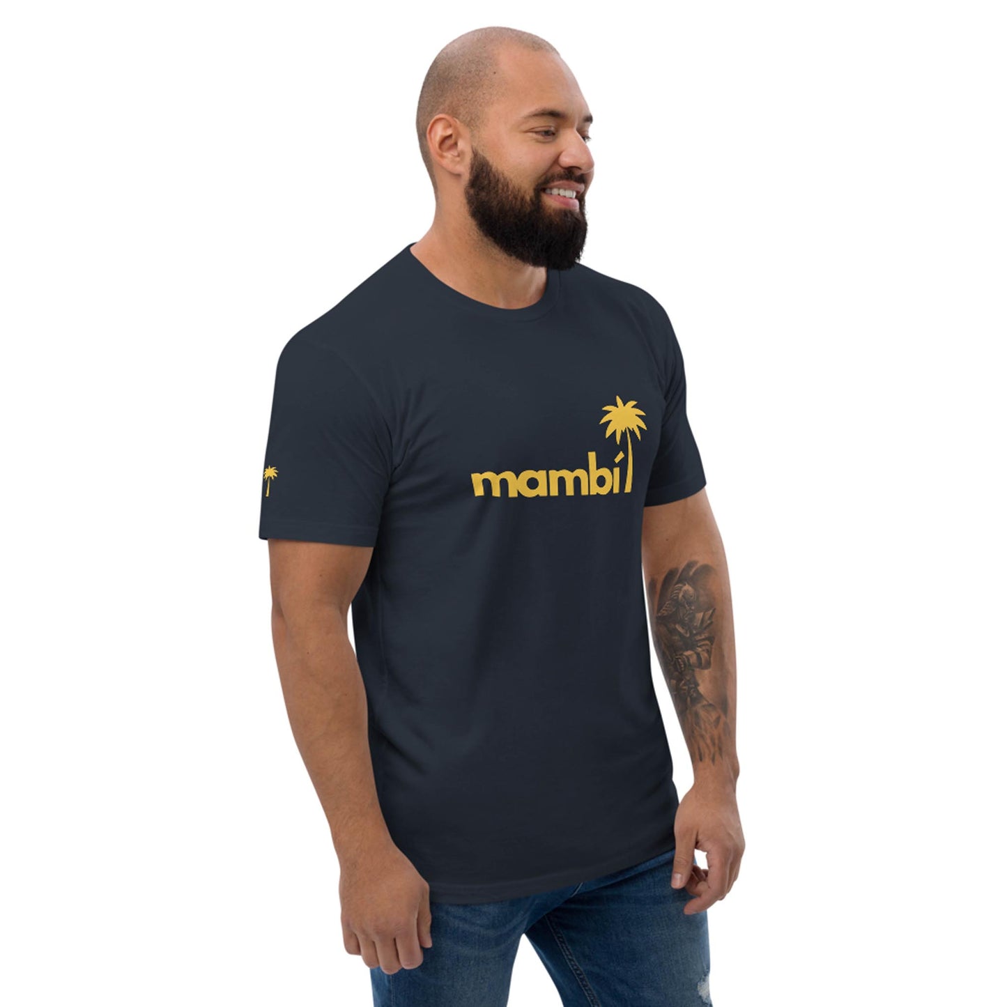 A bearded man smiles while wearing a navy Mambí t-shirt featuring a yellow palm tree graphic on the chest, paired with blue jeans.