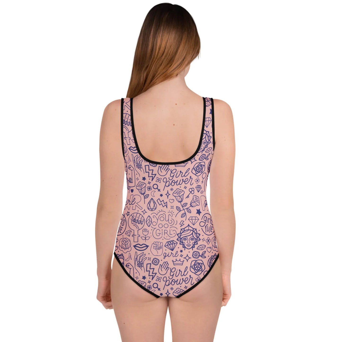A woman with long brown hair stands facing away, wearing a Mambí pink one-piece swimsuit with black trim and girl power themed doodles and phrases printed all over the fabric.